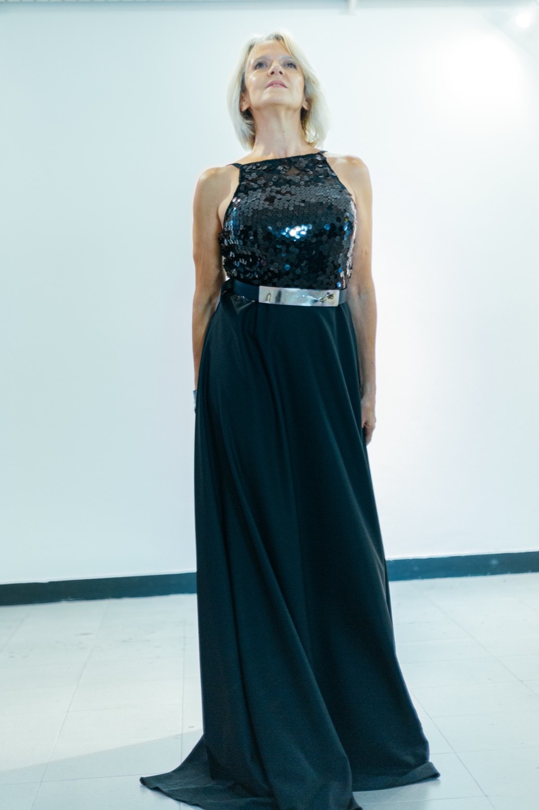 Black sequins and crepe dress con cinturón metálico en la cintura, vista frontal sobre modelo mirando hacia arriba.