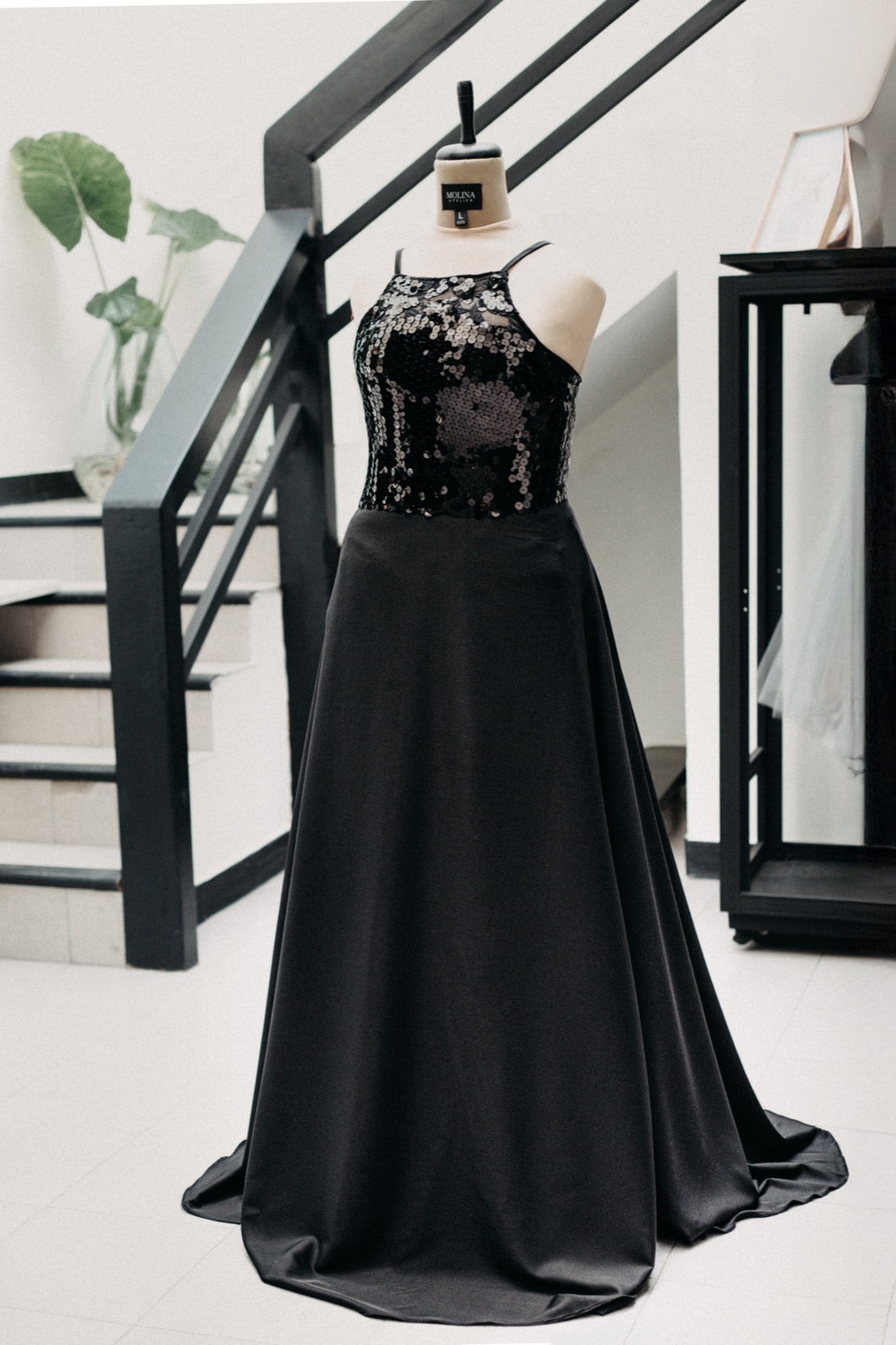 Black sequins and crepe dress, vista frontal completa sobre maniquí junto a una escalera del atelier.