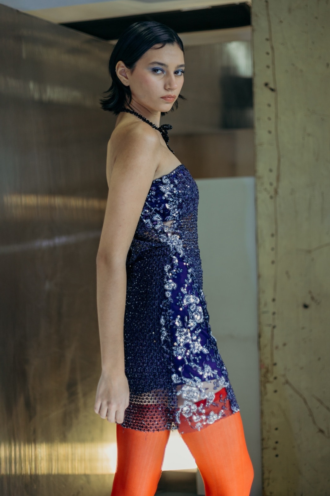 Vestido corto de guipure y tul bordado azul de Atelier Molina, vista de perfil sobre modelo con medias naranjas.