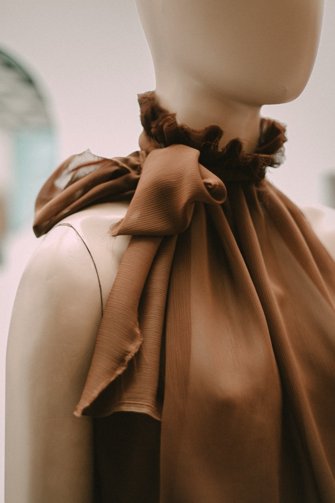 Primer plano del lazo de gasa chocolate anudado sobre el hombro de la blusa, con el volado del cuello fruncido.
