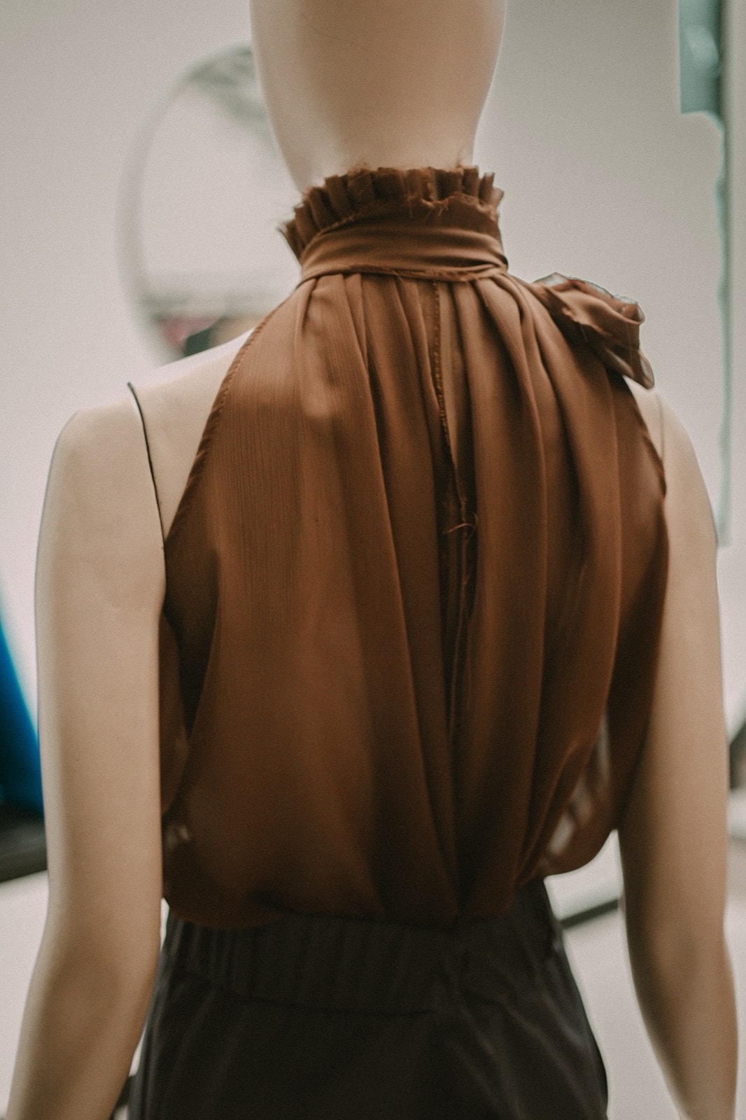 Espalda descubierta de la blusa de gasa bambula chocolate sobre maniquí, con la caída del cuerpo desde el cuello fruncido.