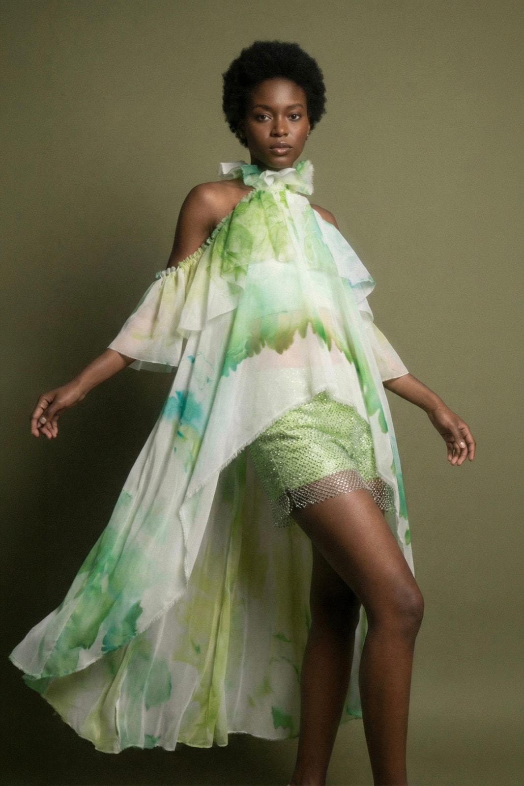 Blusa Olé! Verde sobre modelo de cuerpo entero, con los volados en movimiento sobre fondo verde oliso y short a la vista.