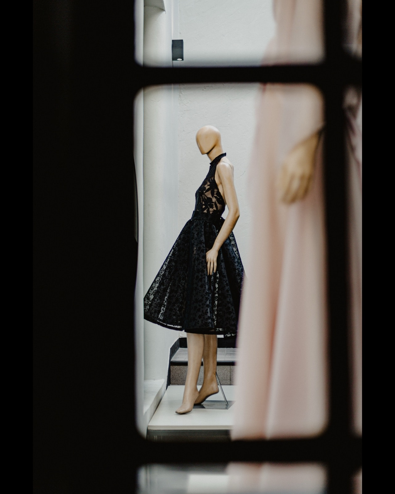 Body de encaje negro con cuello alto, vista de perfil sobre maniquí, enmarcado en el vano de una puerta del atelier.