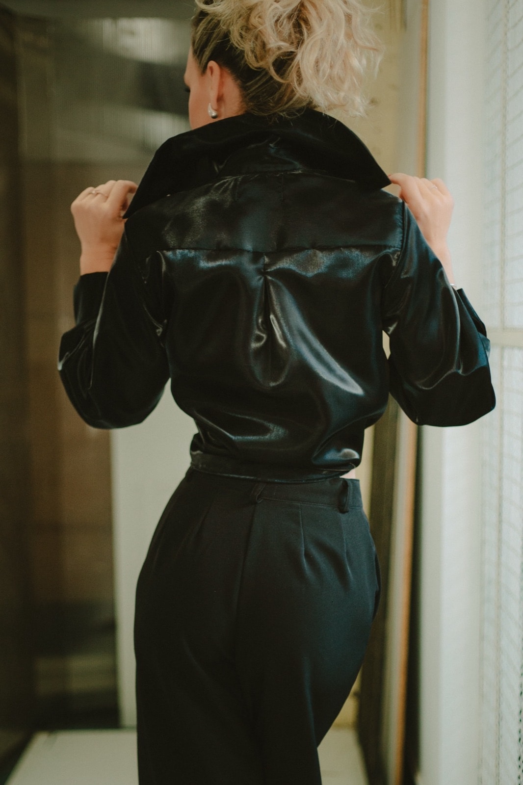 Camisa de organdí negra sobre modelo, vista de espalda con el cuello levantado y la mano sosteniendo la solapa.
