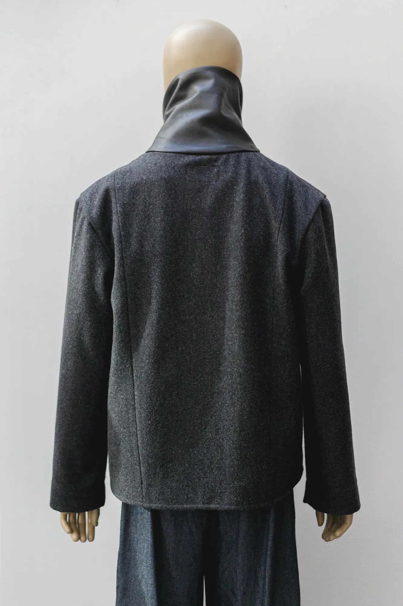 Detalle de espalda del cuello alto en cuero napa negro de la chaqueta de lana prensada gris.