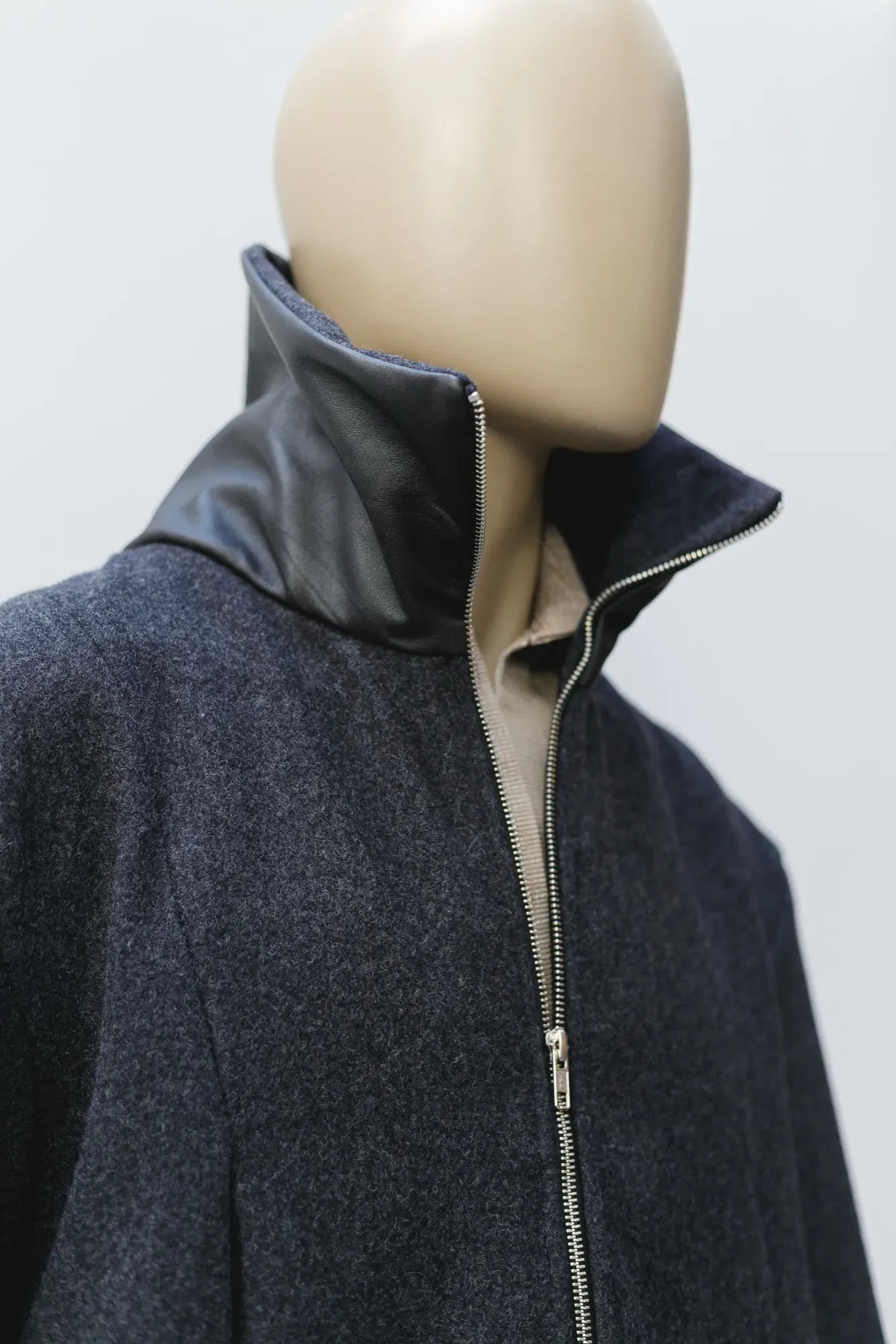 Primer plano del cuello de cuero napa sobre el paño de lana gris de la chaqueta, con camisa beige asomando por dentro.