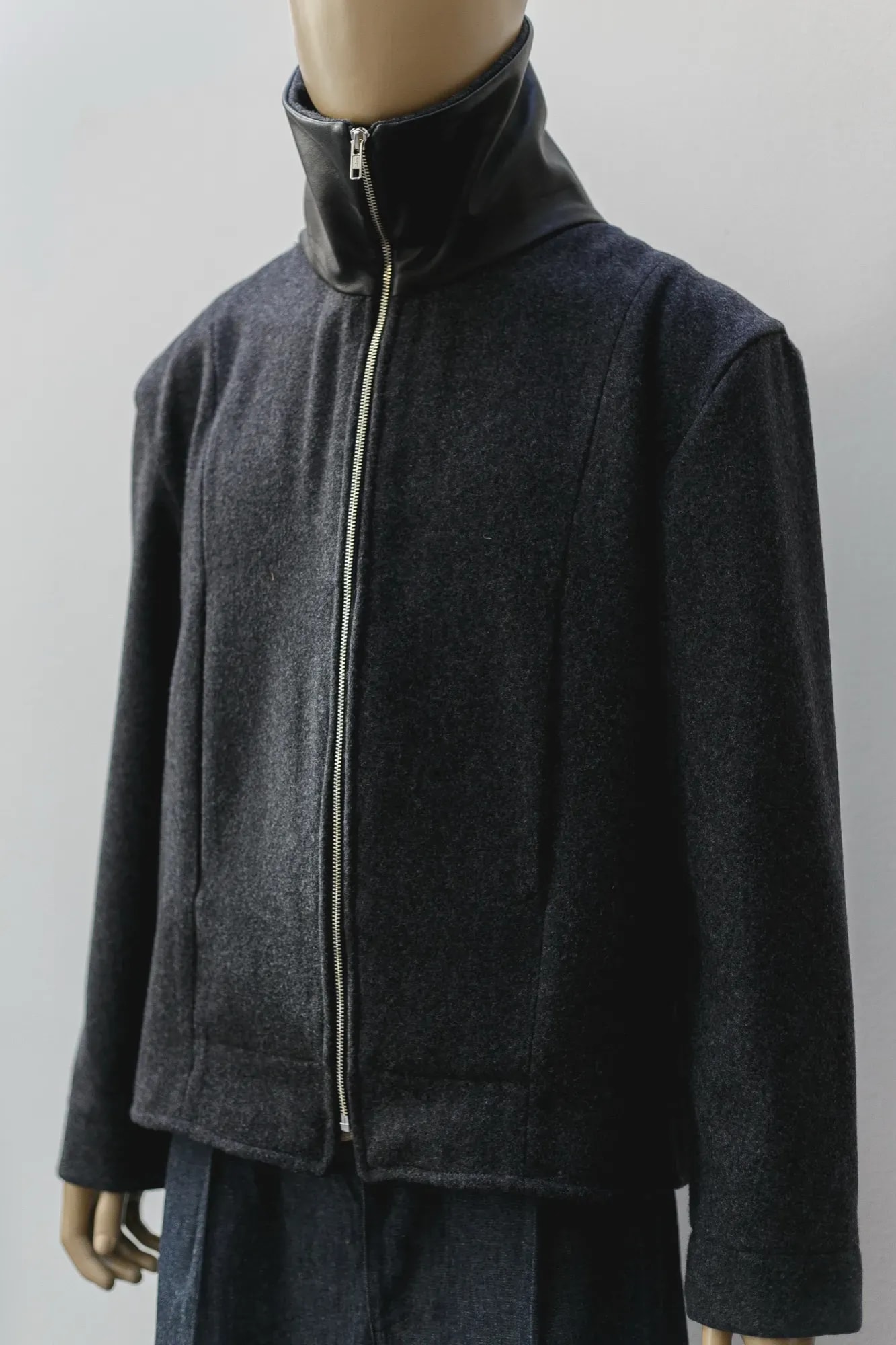 Chaqueta de lana prensada gris de Atelier Molina sobre maniquí, vista de tres cuartos con el cuello de napa negra levantado y el cierre abierto.