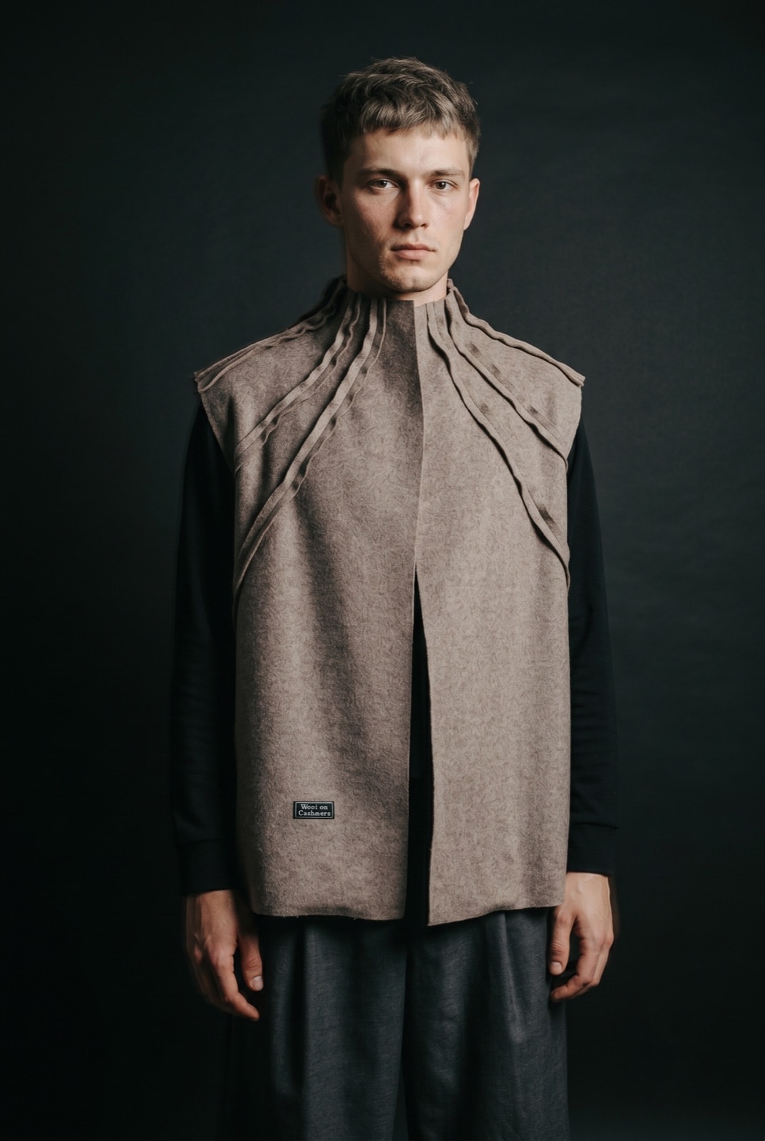 Chaleco de lana y cashmere gris topo de Atelier Molina, con cuello alto de costuras expuestas y abertura frontal, sobre modelo de frente.
