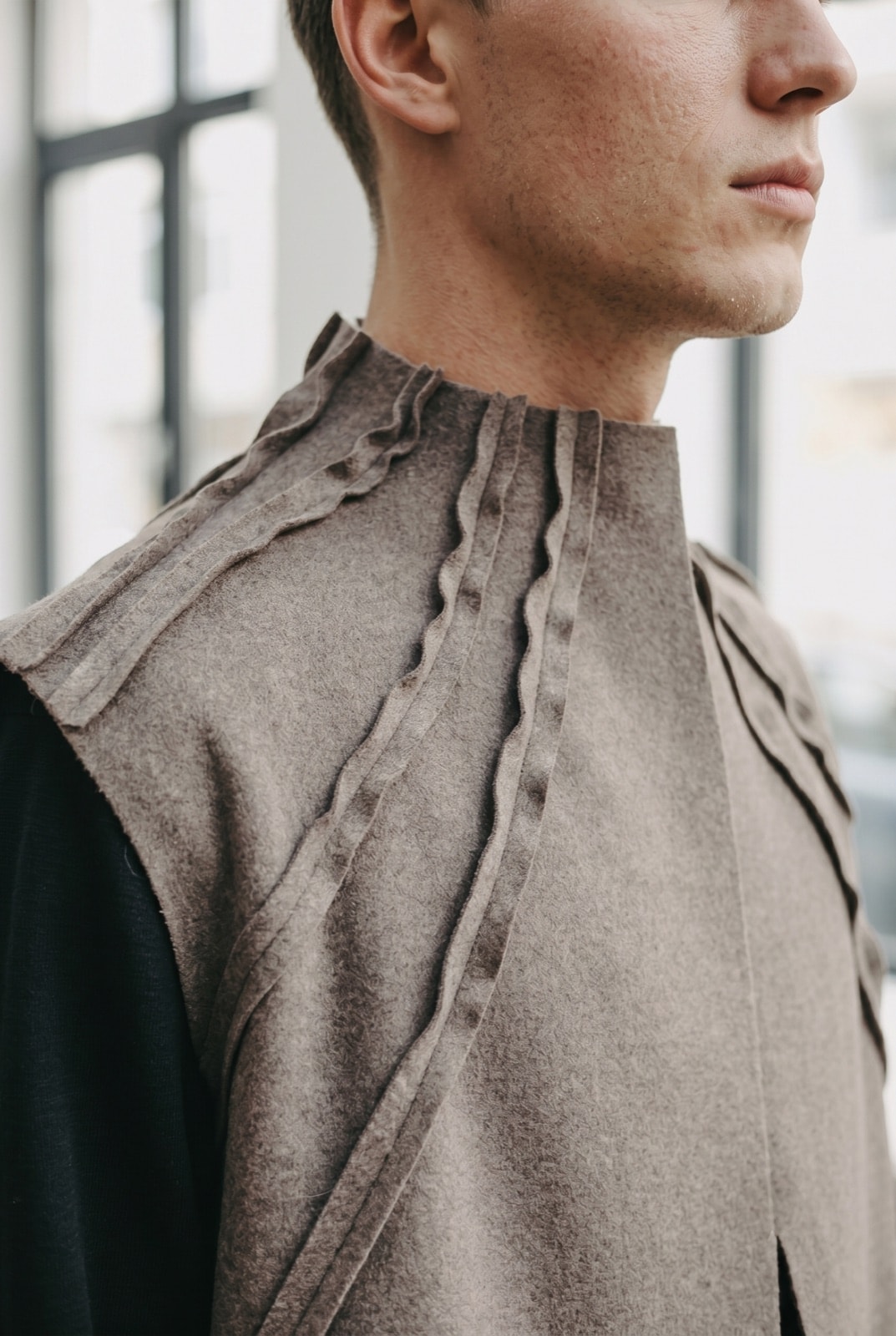 Detalle de perfil del cuello alto del chaleco de cashmere, mostrando las costuras expuestas plisadas que suben hacia el mentón.