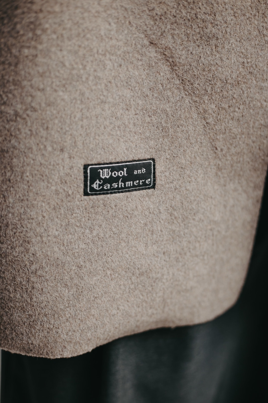 Primer plano de la tela de lana y cashmere gris topo con la etiqueta interior Wool and Cashmere cosida sobre el faldón.