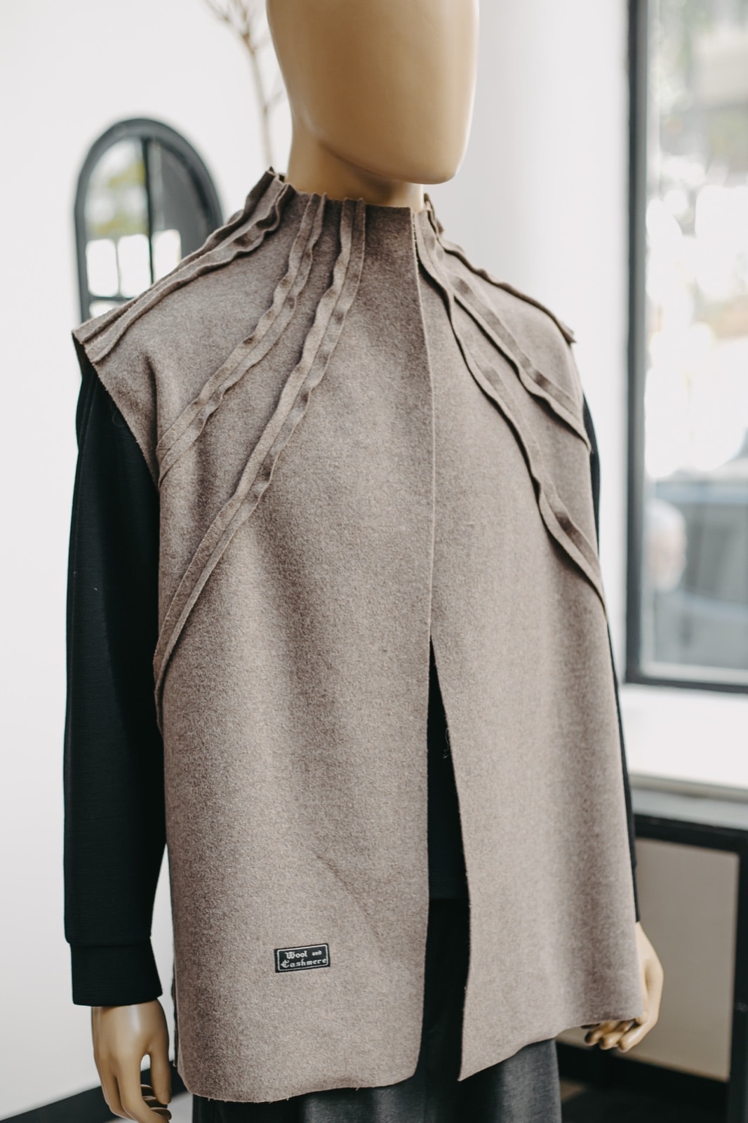 Chaleco de cashmere gris topo sobre maniquí, vista de tres cuartos que muestra la caída recta y la abertura central delantera.