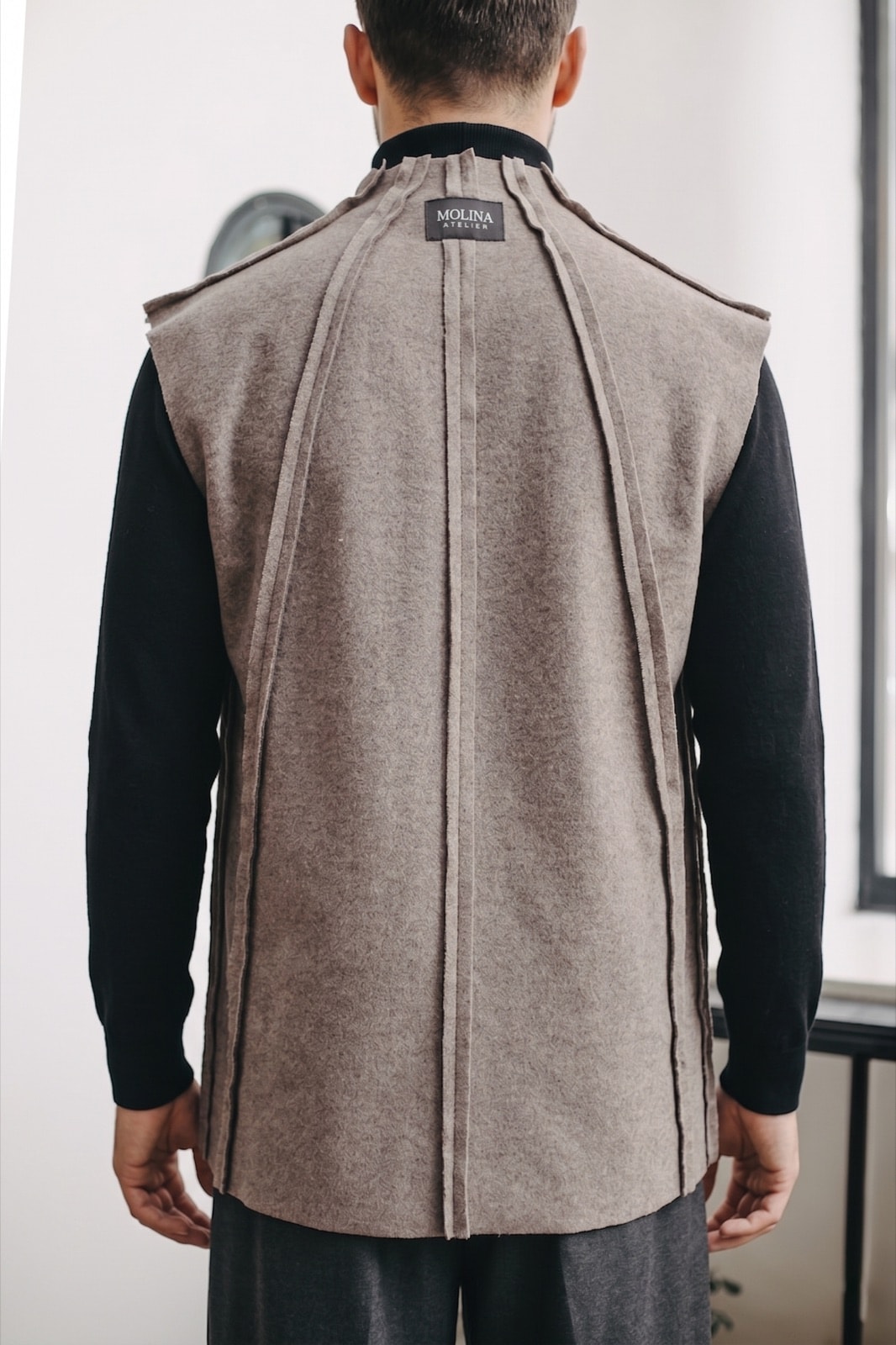 Espalda del chaleco de cashmere sobre modelo, con la etiqueta Molina Atelier visible en la base del cuello y las costuras expuestas centrales.