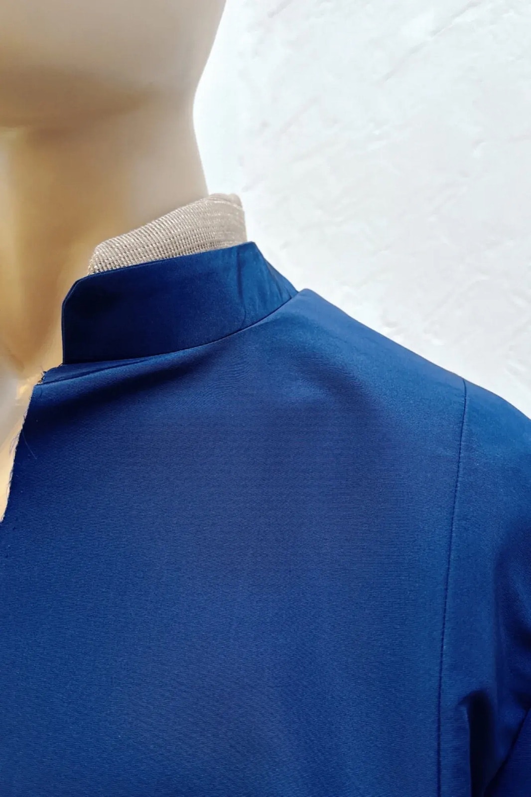 Detalle del cuello mao de la chaqueta de gros de seda azul Klein sobre maniquí, con vista lateral de la costura del hombro.