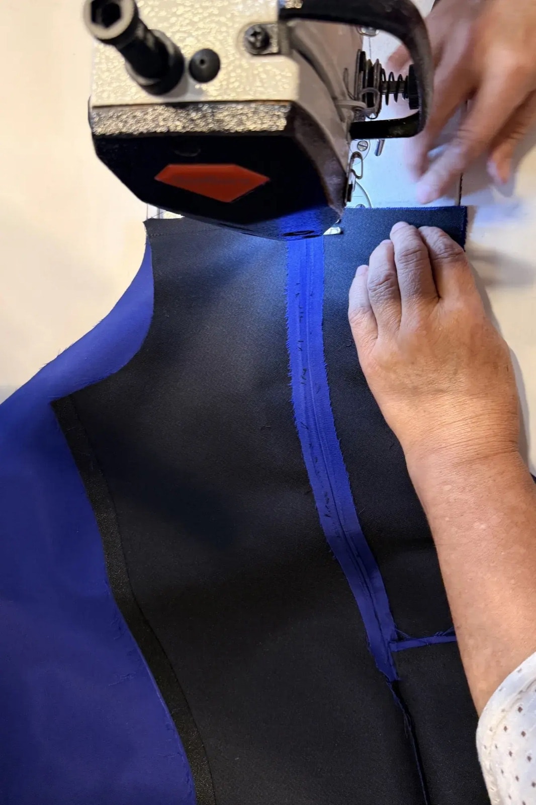 Confección artesanal de la chaqueta azul Klein en el taller, con la costura del cierre frontal en proceso sobre la máquina overlock.