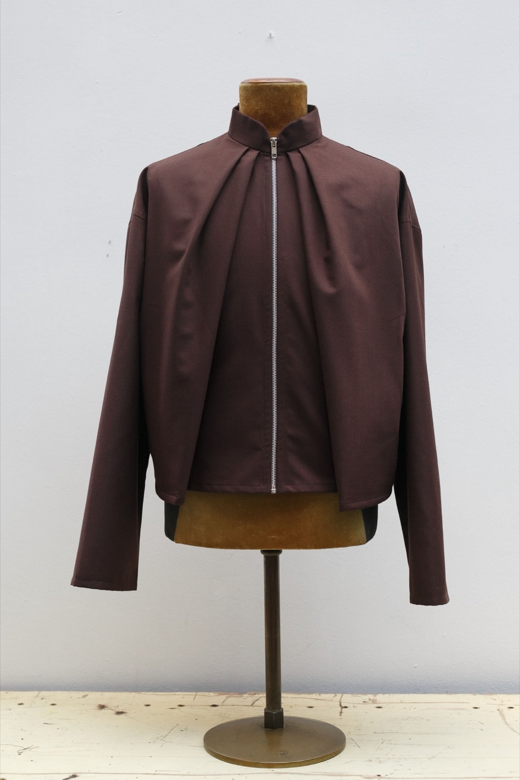 Campera de casimir marrón sobre maniquí, vista delantera con cuello alto, pliegues frontales y cierre metálico visible, fondo claro.