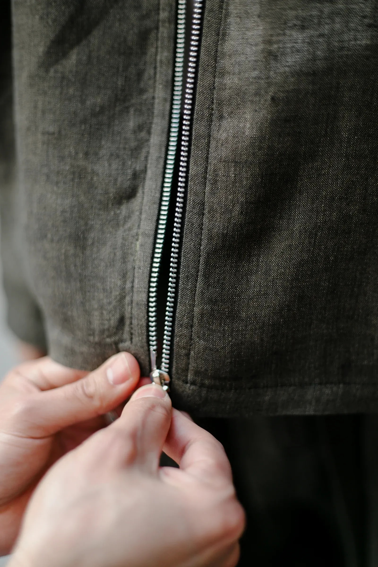 Detalle del cierre metálico de doble carro de la Chaqueta Molina de lino italiano verde alga, abriéndose desde el ruedo. Atelier Molina, Buenos Aires