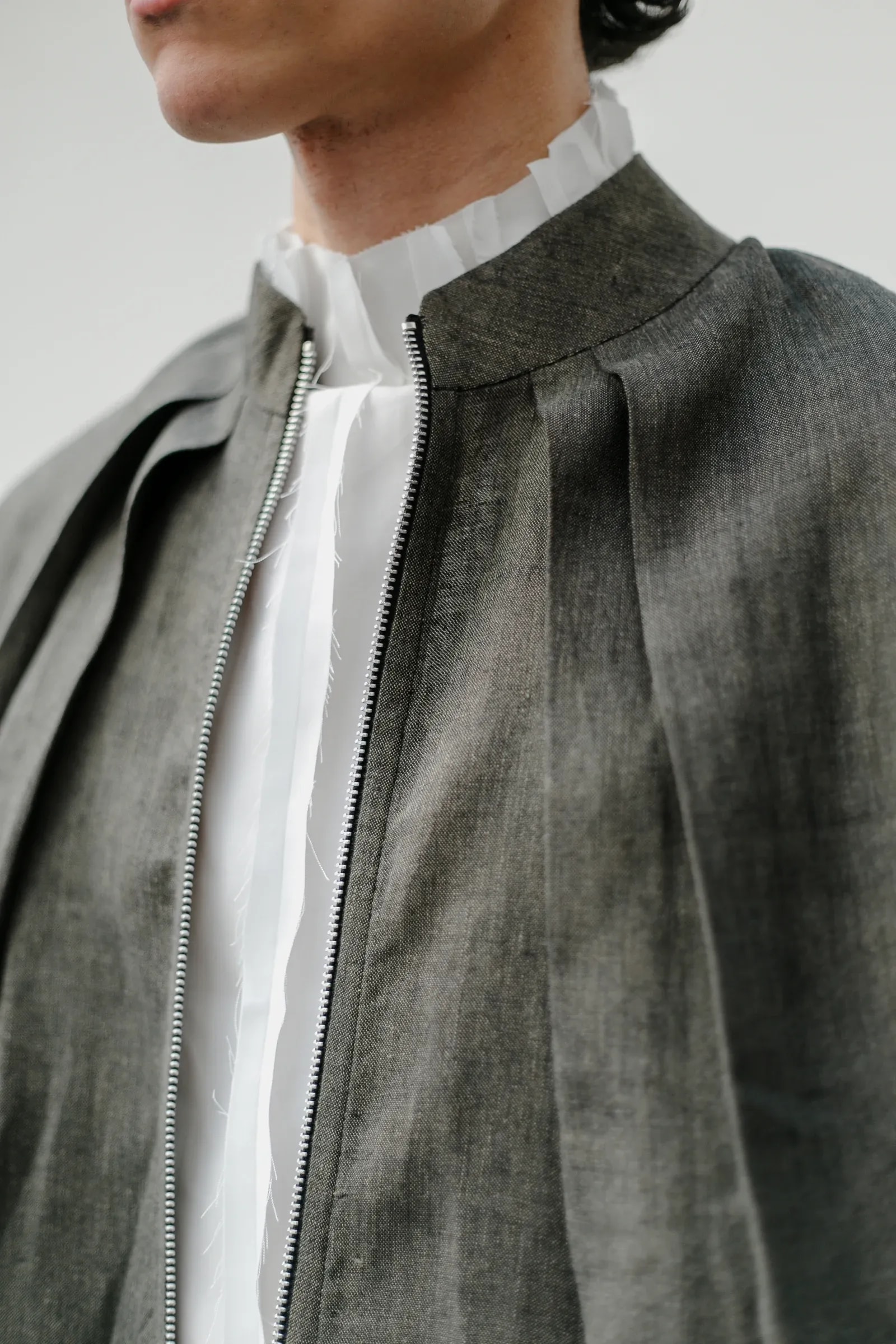 Detalle del cuello mao y los pliegues del hombro de la Chaqueta Molina de lino italiano verde alga, con el cierre de doble carro y el cuello deshilachado de la Camisa Radial debajo. Atelier Molina, Buenos Aires
