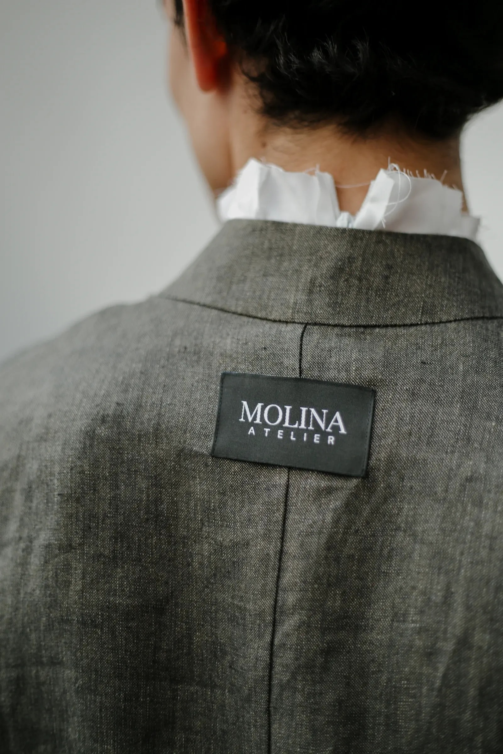 Espalda de la Chaqueta Molina de lino italiano verde alga, con la etiqueta Molina Atelier cosida al centro y la costura que parte la espalda al medio. Atelier Molina, Buenos Aires