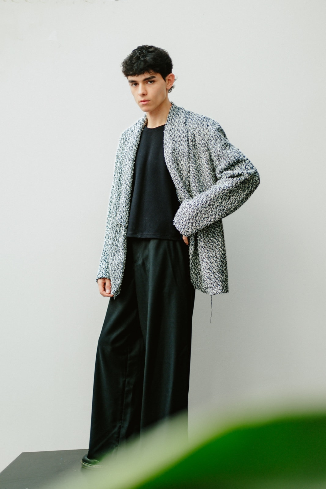 Chaqueta de tweed de algodón con pantalón sastrero negro de pierna ancha, de cuerpo entero y de tres cuartos, con una mano en la cintura.