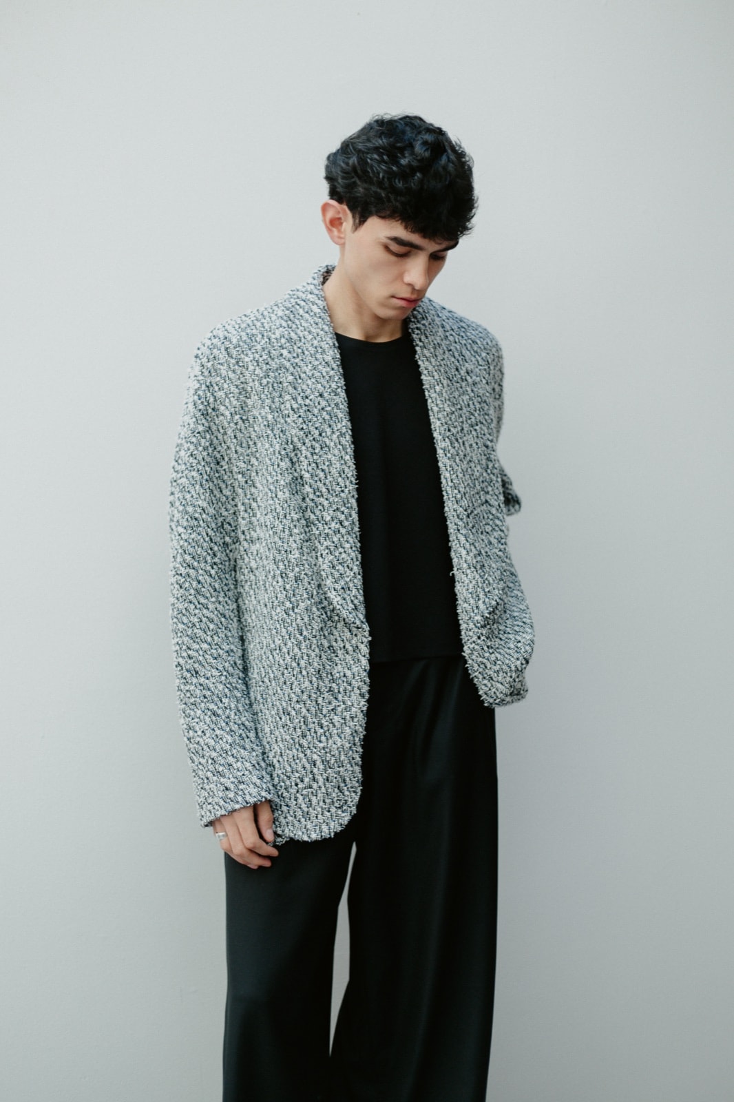 Chaqueta de tweed blanco y negro con cuello chal, vista de frente y apenas de costado, con una mano en el bolsillo del pantalón negro.