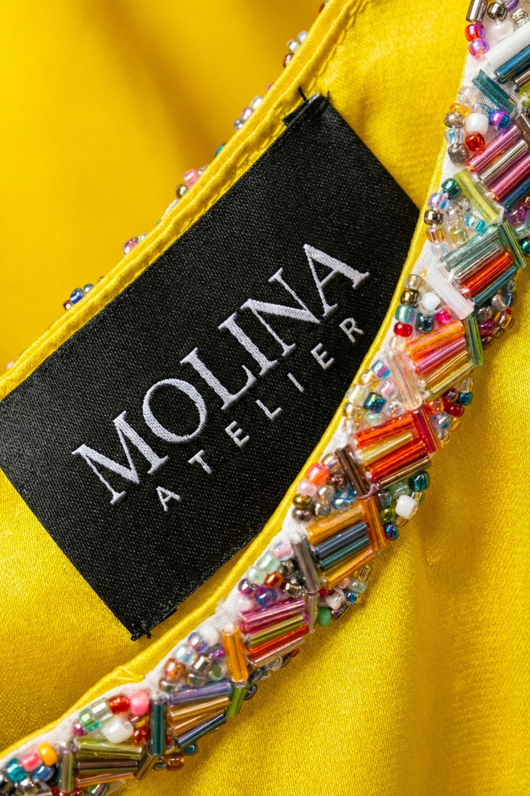 Detalle de la etiqueta Molina Atelier junto al cuello bordado con cuentas multicolor del croptop amarillo de satén.