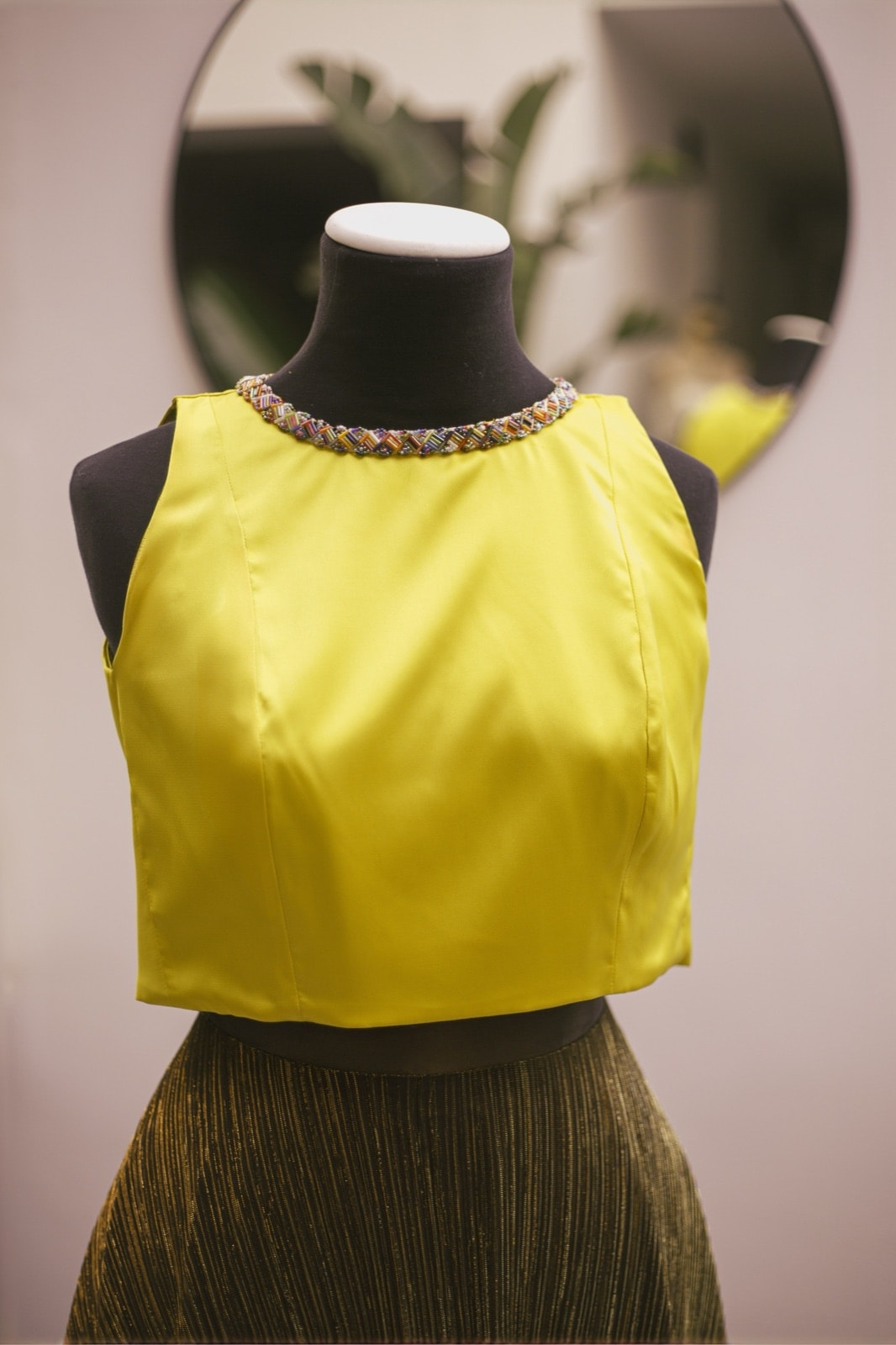 Croptop amarillo con cuello bordado en cuentas multicolor, vista frontal sobre busto, con falda oscura debajo.
