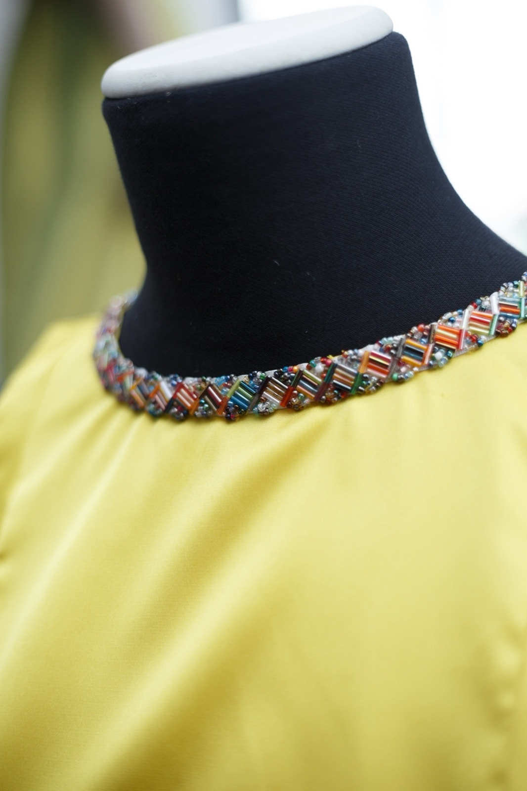 Detalle del cuello bordado con cuentas multicolor del croptop amarillo de satén de seda, primer plano sobre busto.