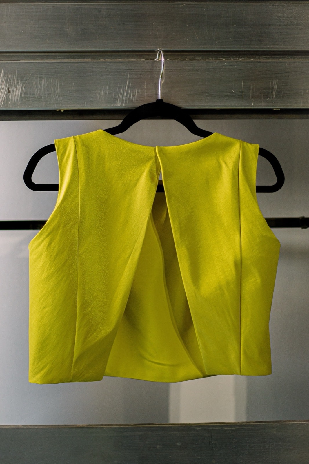 Espalda del croptop de tafetán color lima de Atelier Molina, colgado en percha, mostrando la abertura posterior en punta.