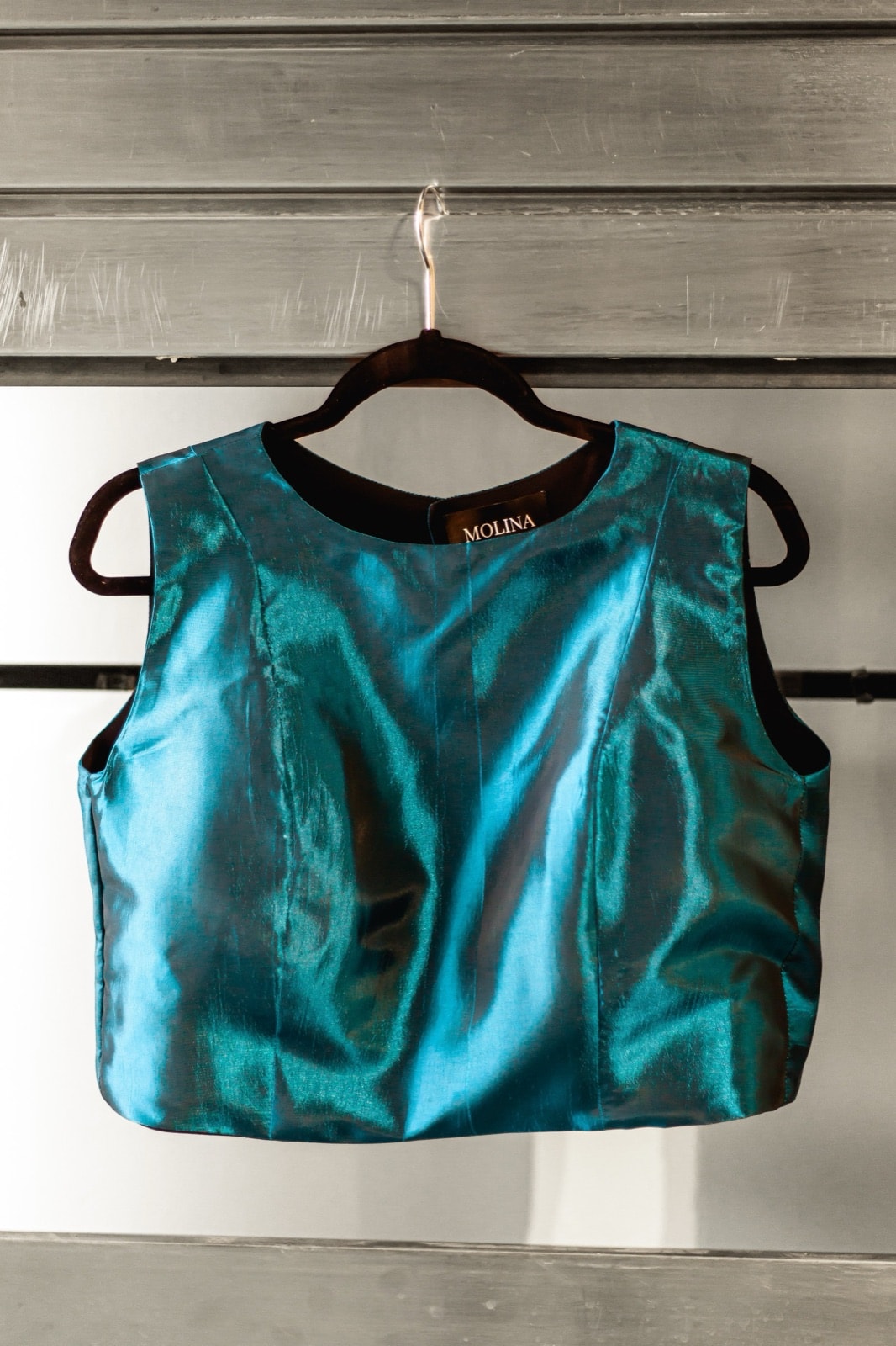 Croptop de tafetán petróleo de Atelier Molina en percha, vista frontal colgado sobre un fondo de madera gris.