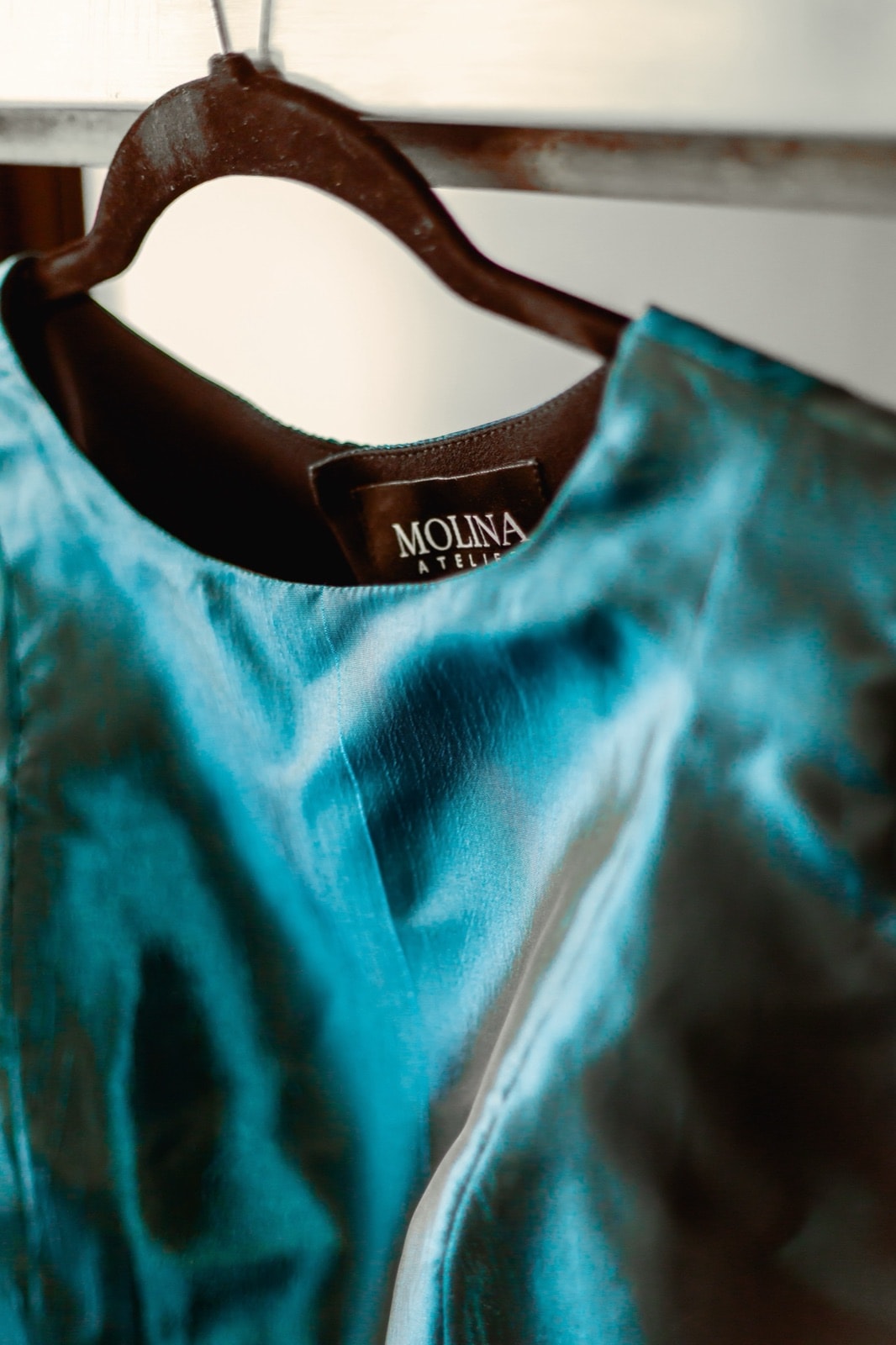Detalle del cuello y la etiqueta Molina Atelier del croptop de tafetán petróleo, colgado en percha.