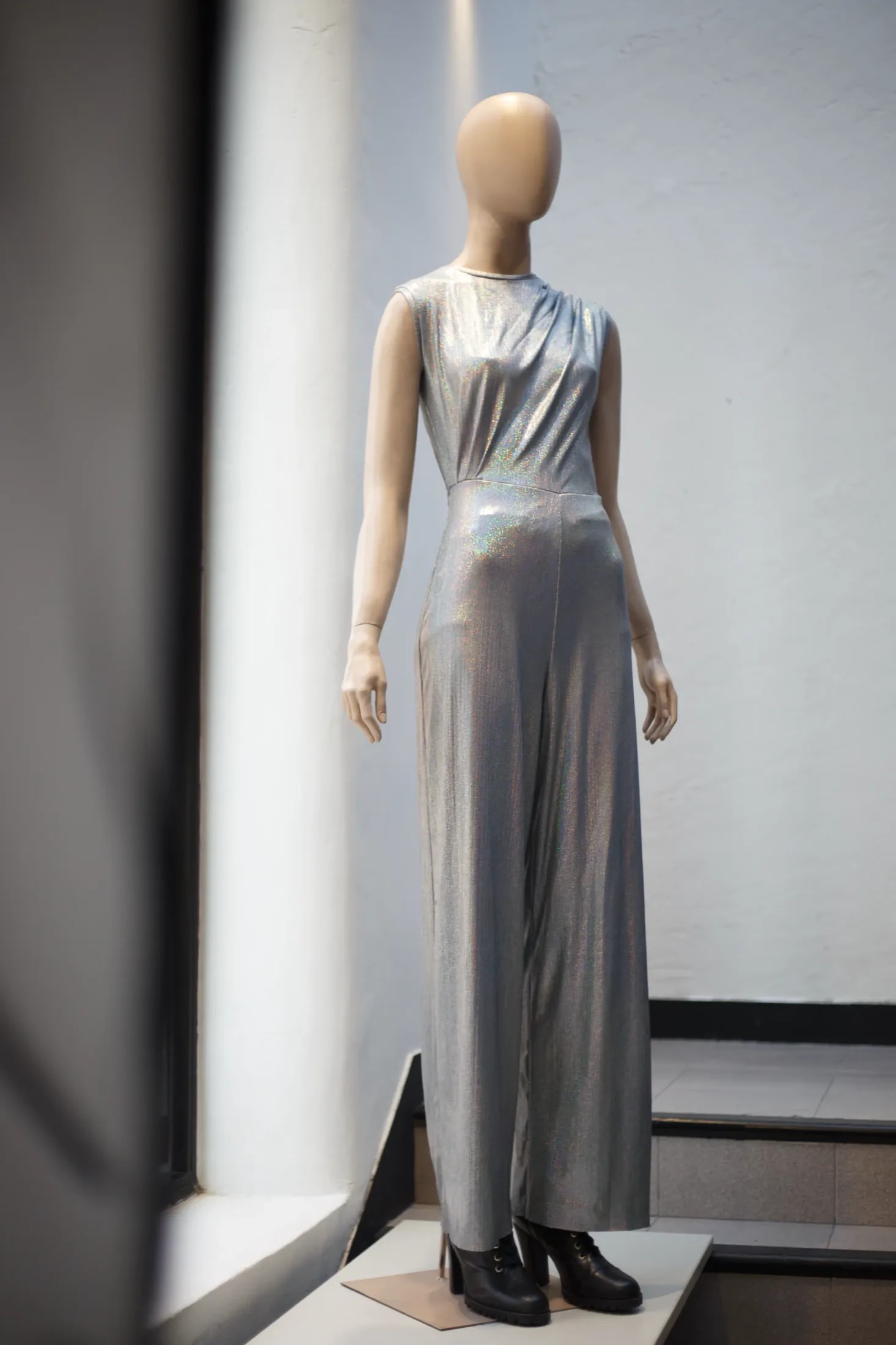Mono plateado holográfico sobre maniquí en la vidriera del showroom, vista delantera completa con pantalón ancho hasta el piso.