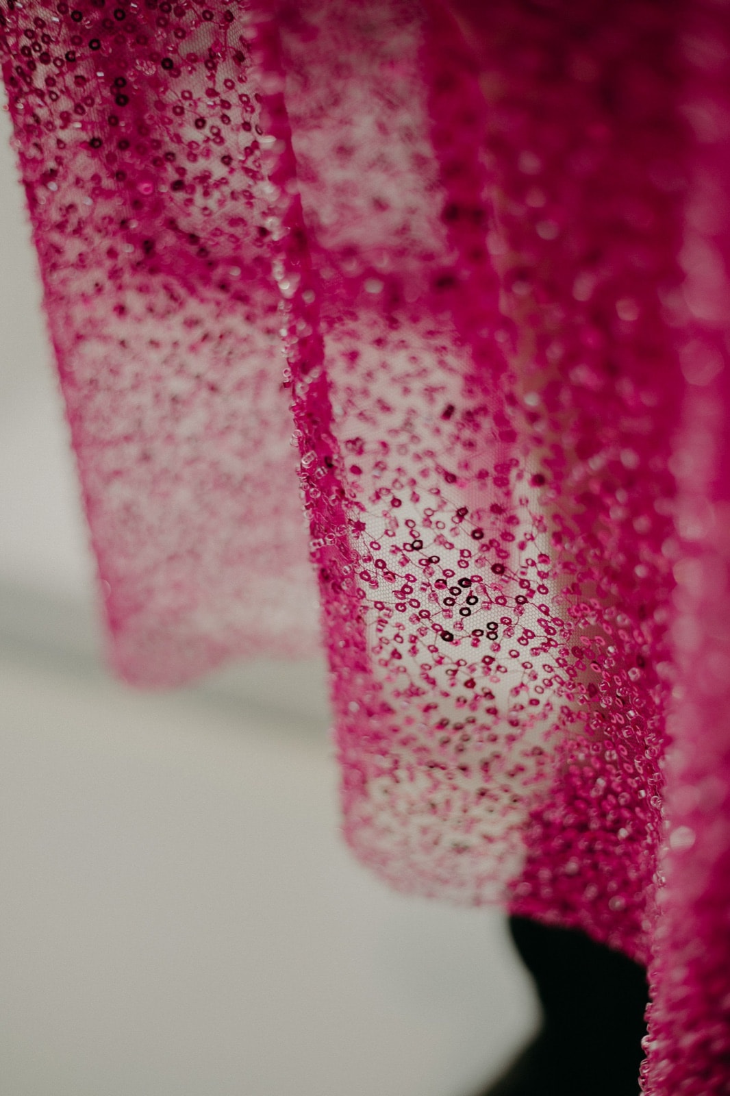 Primer plano del bordado de canutillos y lentejuelas fucsia sobre malla, con la luz atravesando la trama semi transparente.