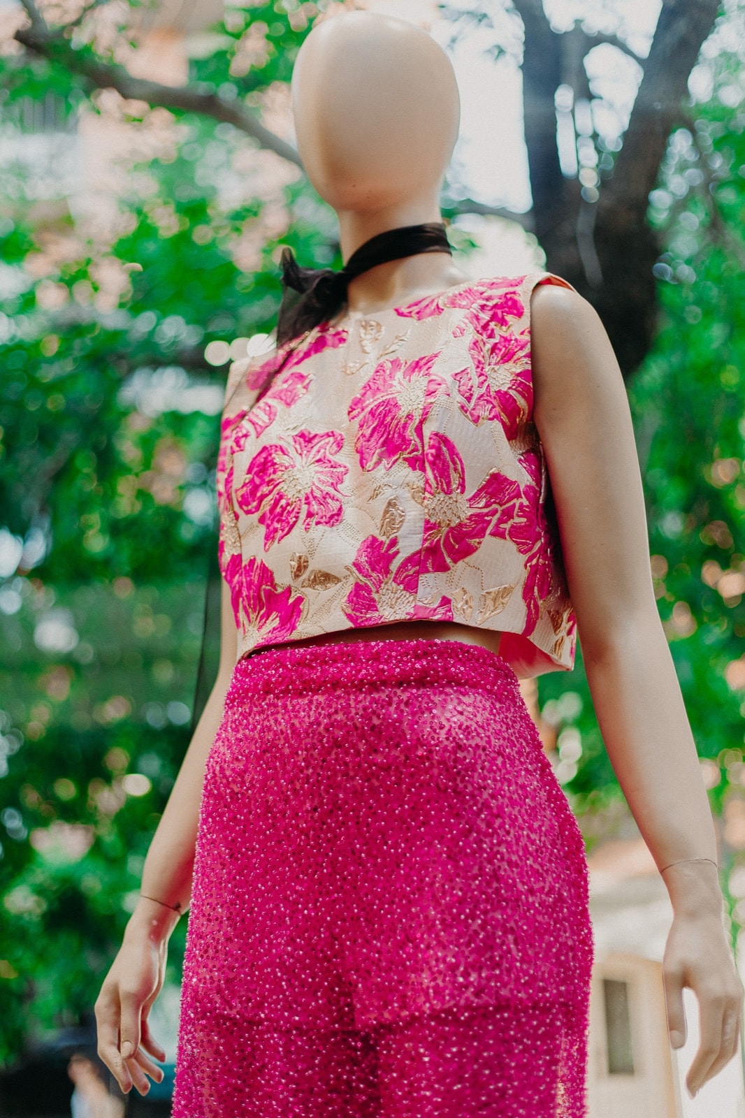 Detalle del top jacquard floral fucsia y dorado sobre la cintura de la falda bordada, con el follaje de la calle de fondo.