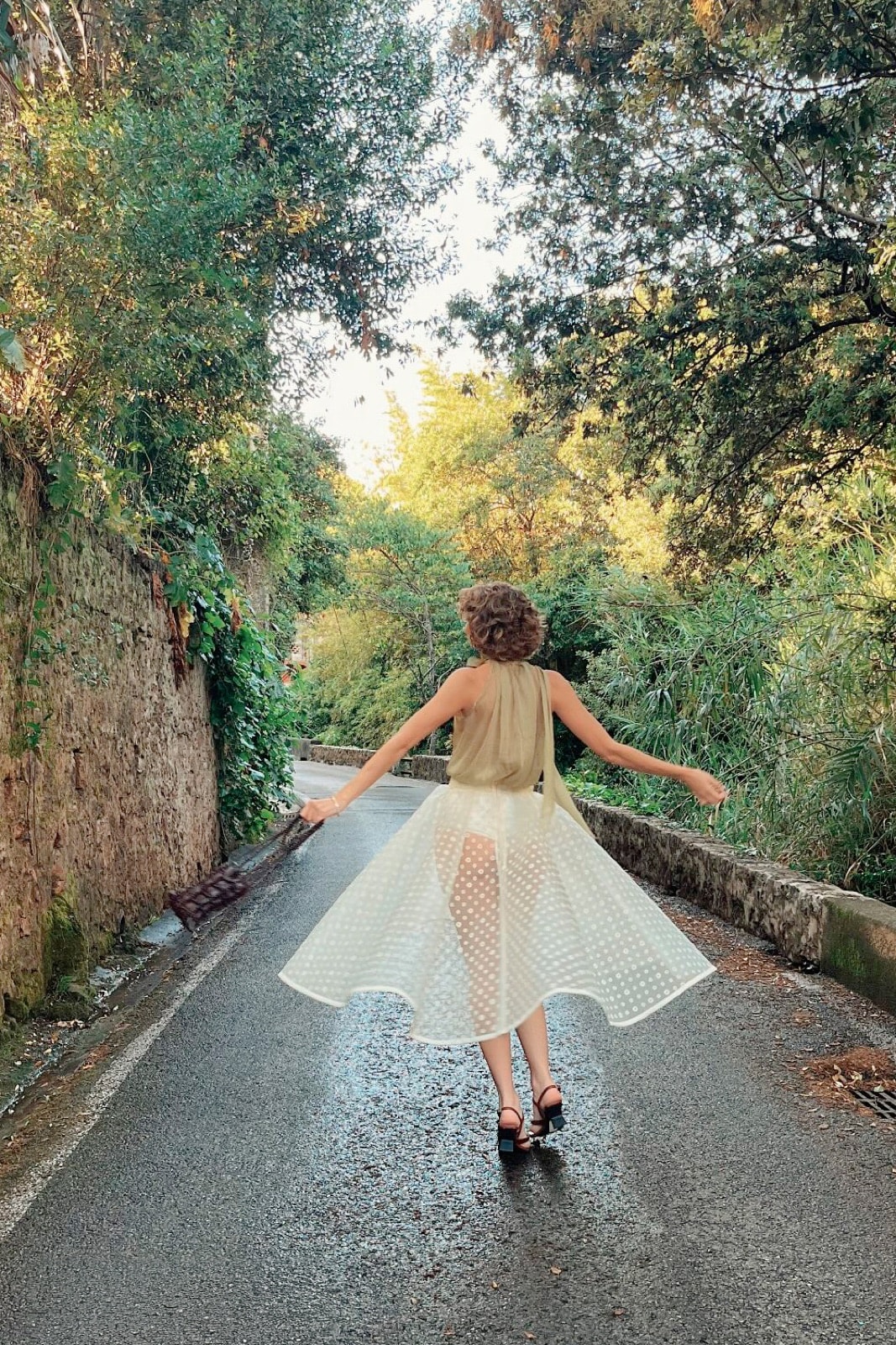 Falda de Villoné Crema de Atelier Molina sobre modelo de espaldas caminando por un camino arbolado, con la prenda en pleno vuelo.