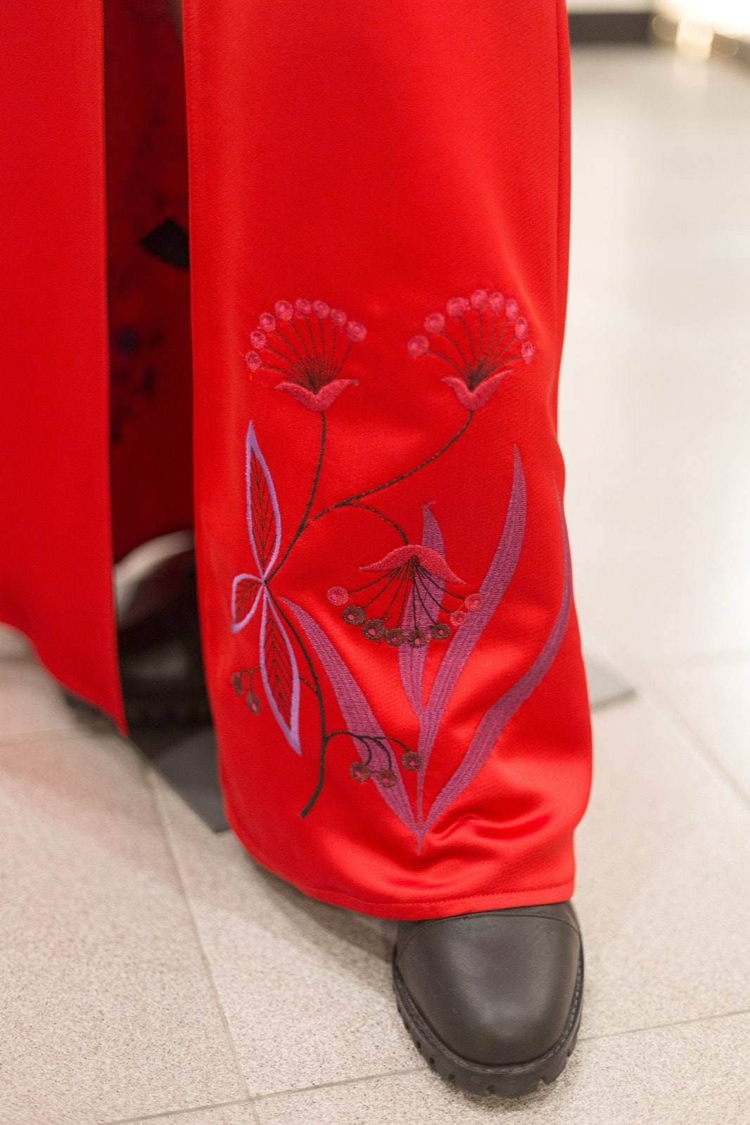 Detalle del bordado floral en tonos rosa y violeta a la altura del ruedo de la falda roja, junto a una bota negra.