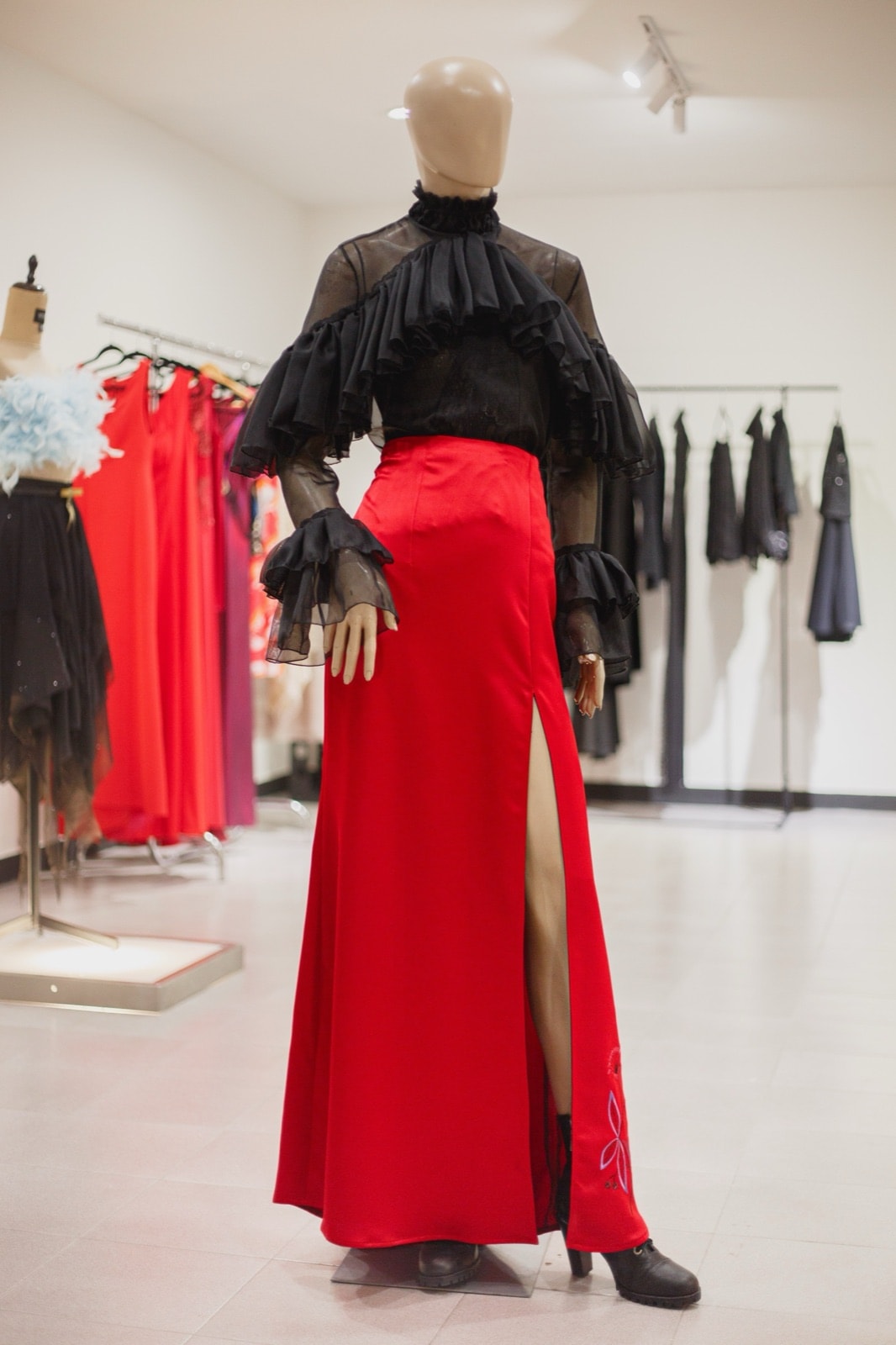 Falda roja bordada con abertura frontal sobre maniquí en el showroom, combinada con blusa negra de tul y volados en las mangas.