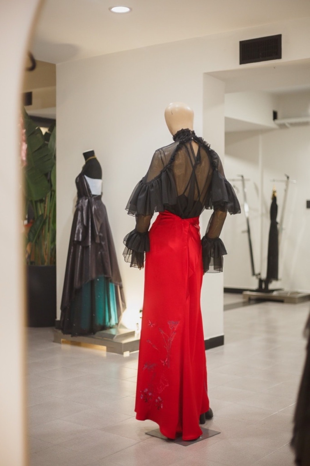 Vista trasera de la falda roja bordada sobre maniquí, con el bordado de mariposas y ramas descendiendo por la parte posterior.