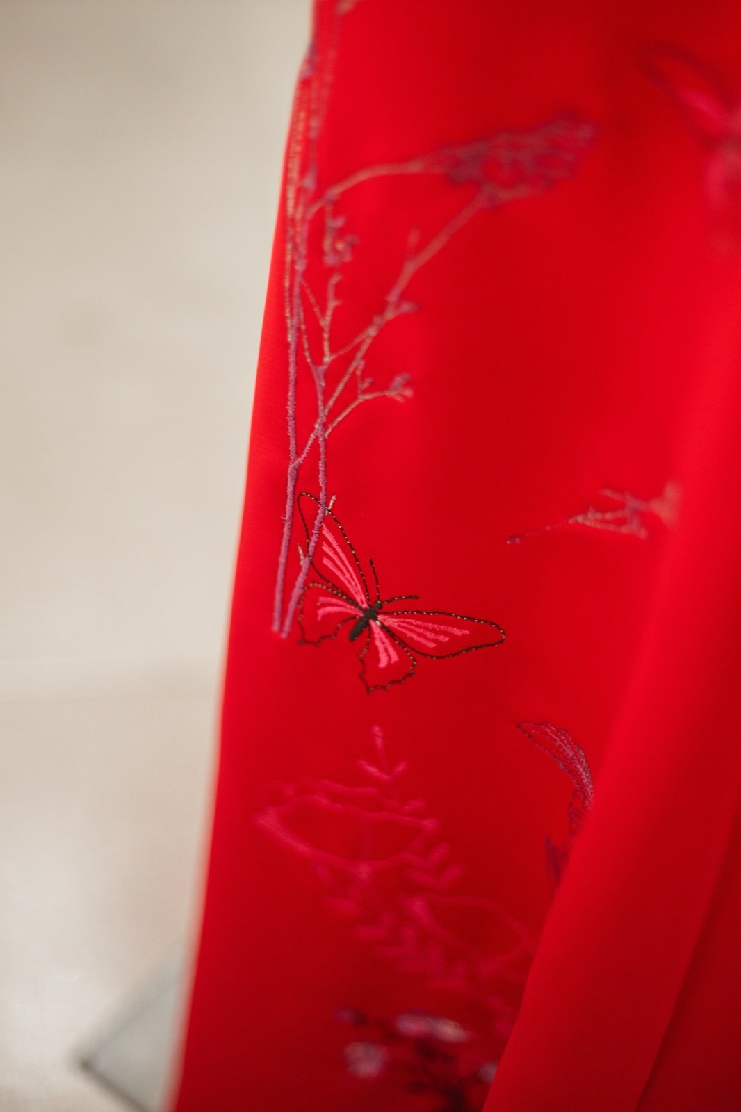 Primer plano del bordado de una mariposa y ramas finas sobre el raso rojo de la falda, con hilos en tono rosa y negro.