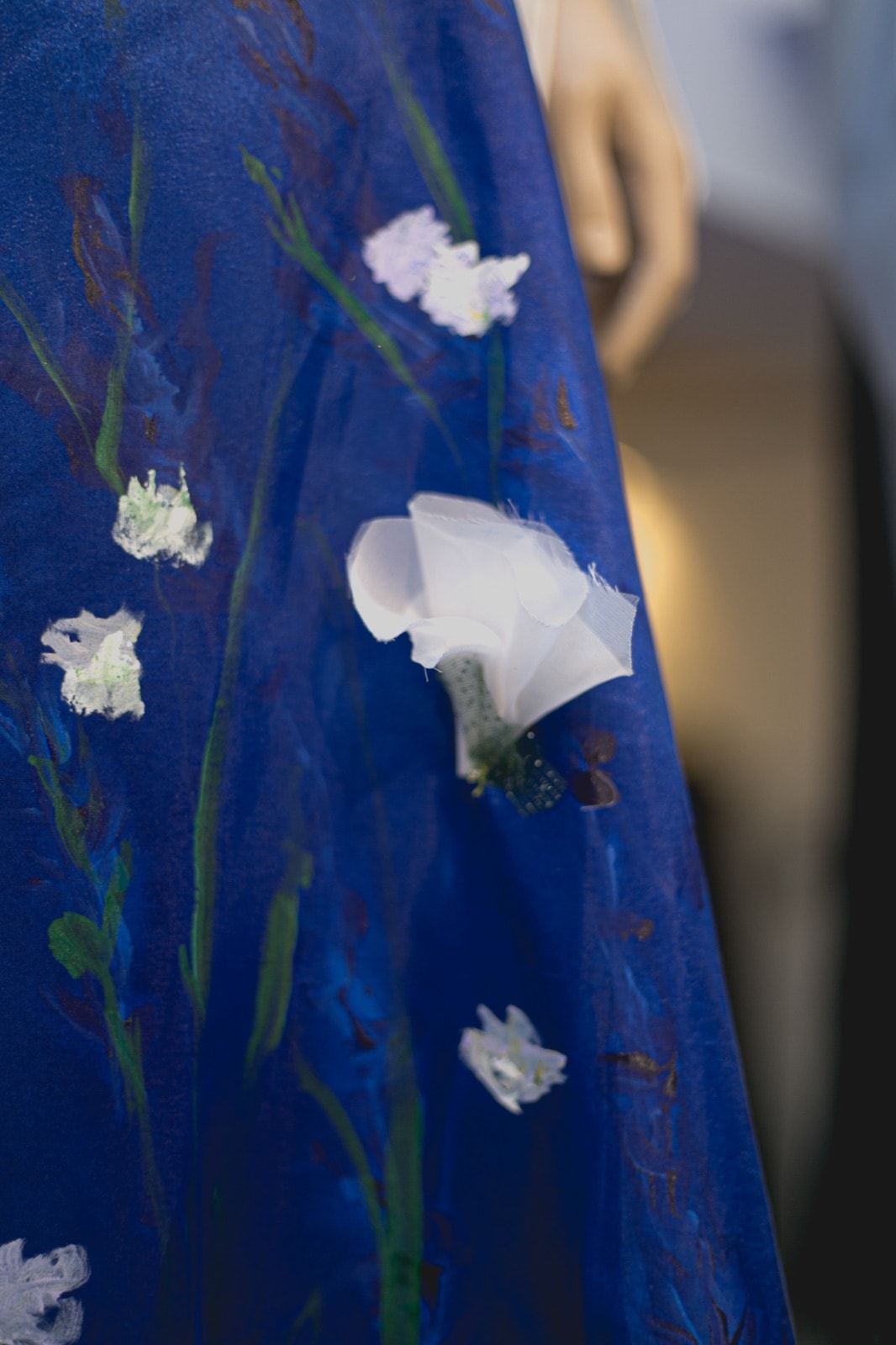 Detalle de una flor de tela en relieve sobre la falda de tafetán azul, entre tallos pintados a mano en verde y blanco.