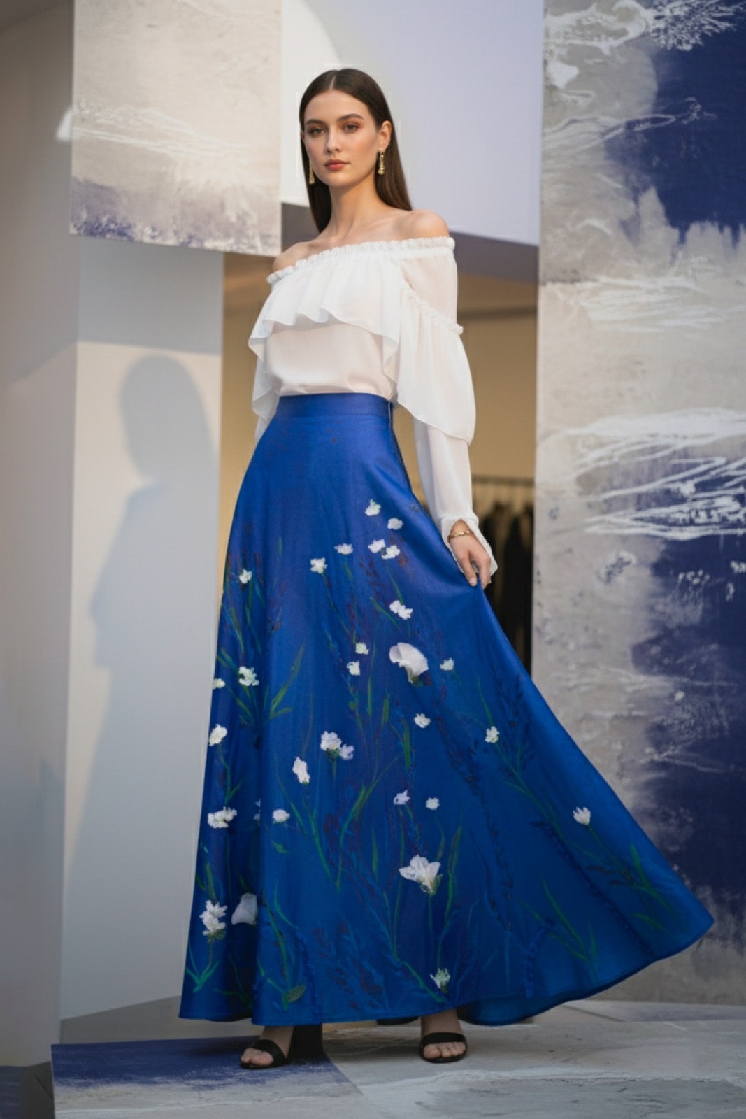 Falda larga de tafetán azul con flores pintadas y bordadas de Atelier Molina, sobre modelo caminando con blusa blanca off shoulder.