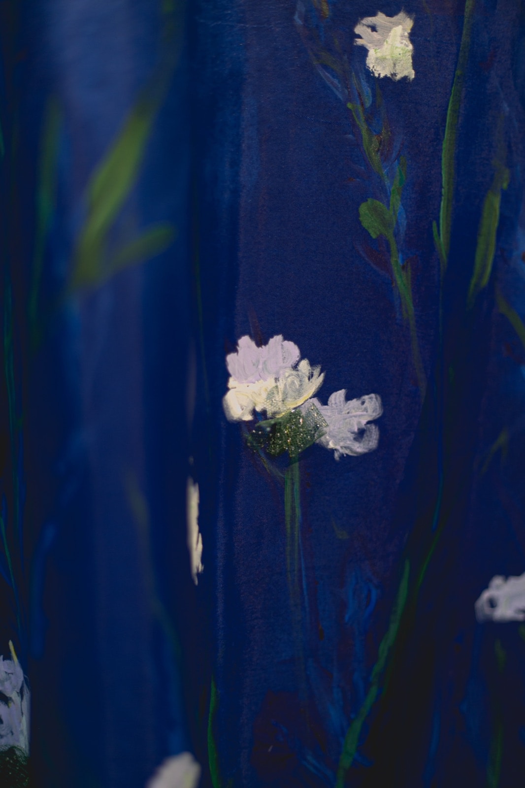 Primer plano de una flor pintada en blanco sobre el tafetán azul de la falda, con el bordado de cristal en el centro.