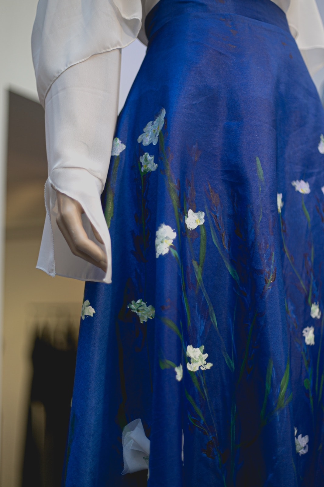 Detalle del ruedo de la falda de tafetán azul junto a la manga de la blusa blanca, mostrando el degradé de tallos pintados.