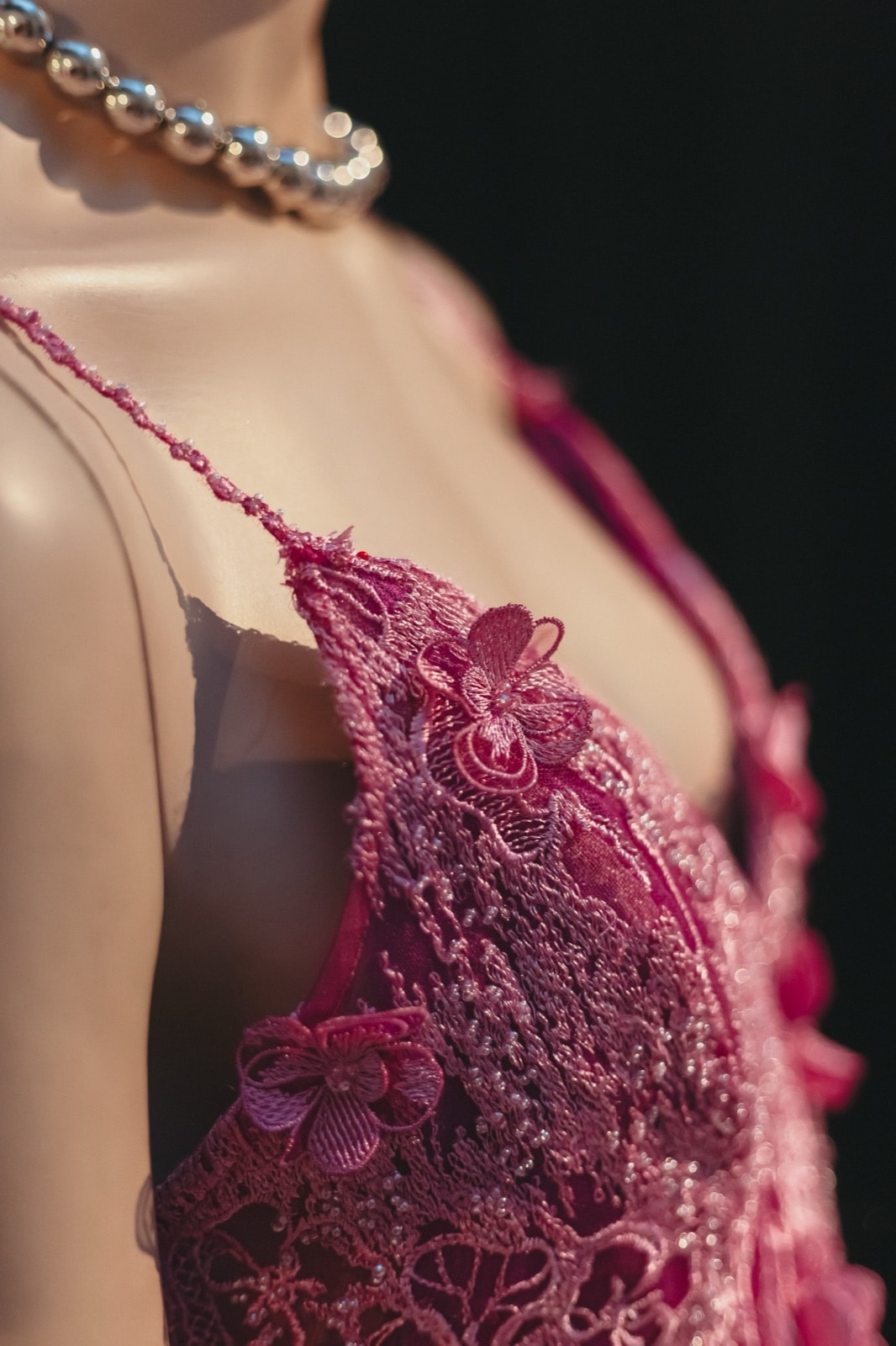 Detalle en primer plano del bordado floral en relieve del corpiño del vestido largo fucsia, sobre maniquí.