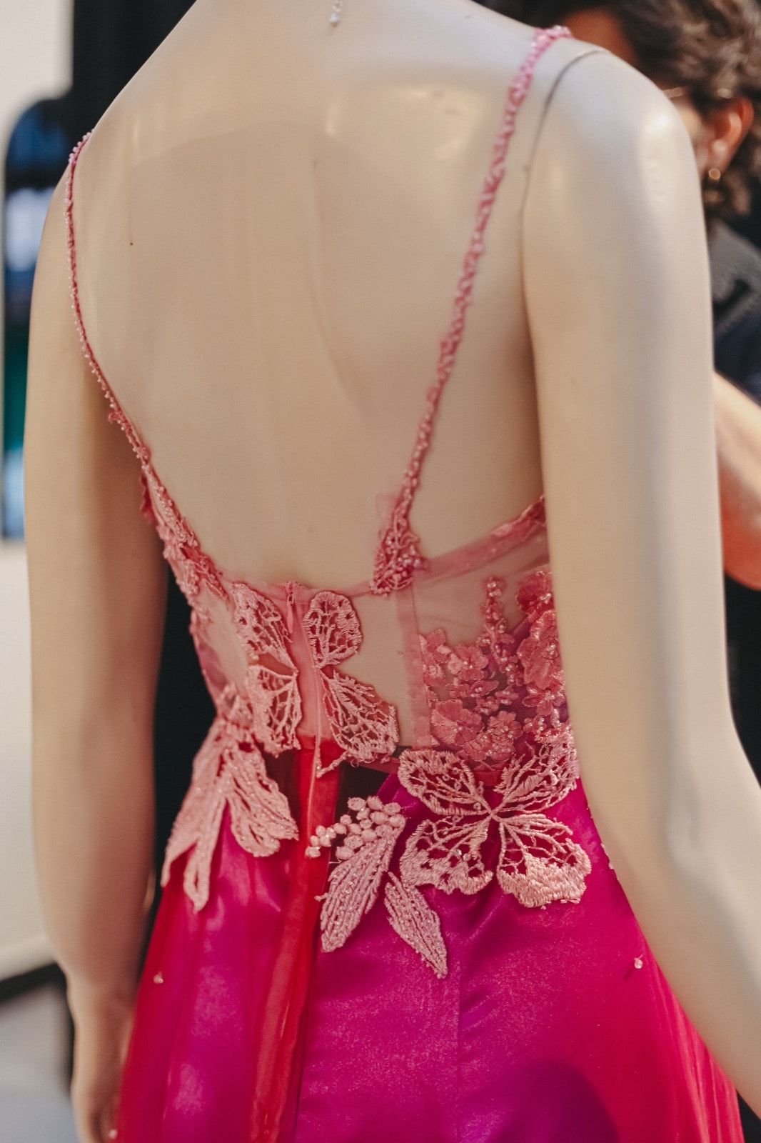 Detalle de espalda del vestido largo fucsia, con tiras finas y bordado floral en relieve sobre tul transparente.