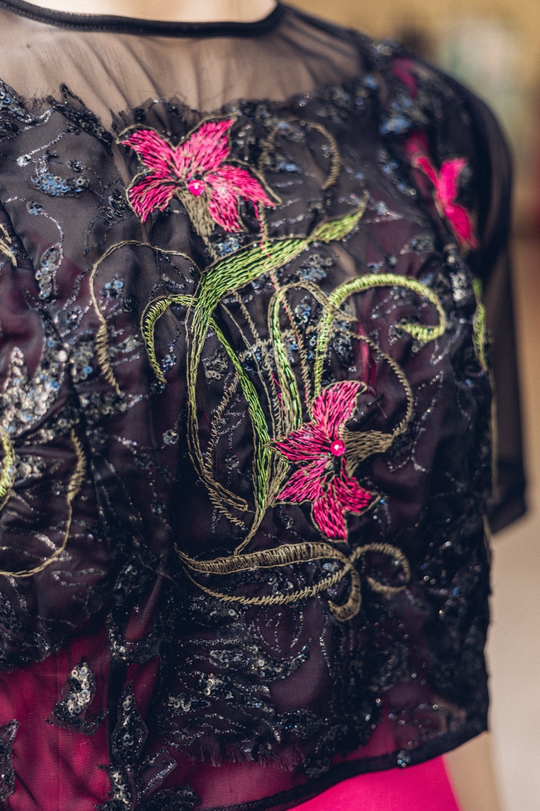 Primer plano del bordado floral fucsia y verde sobre tul negro del croptop Garden Night, con lentejuelas en el fondo.