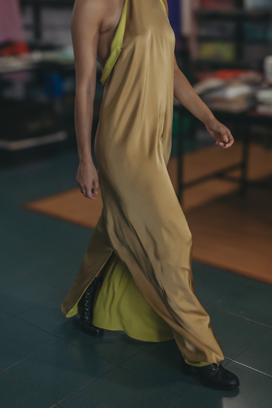 Detalle del ruedo del Golden Lime Dress en movimiento, con la abertura que deja ver el forro lima y botas negras.