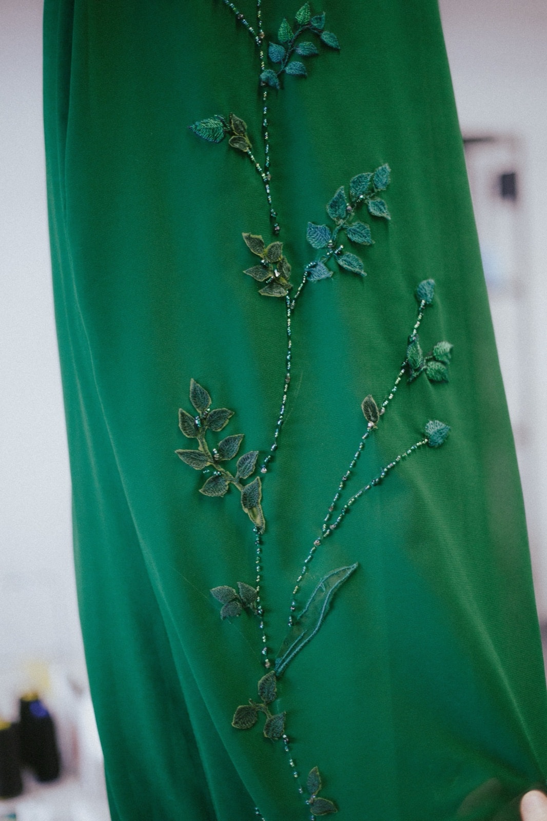 Primer plano del ruedo del vestido verde con el bordado floral en canutillos, mostrando la caída de la gasa acrepada.