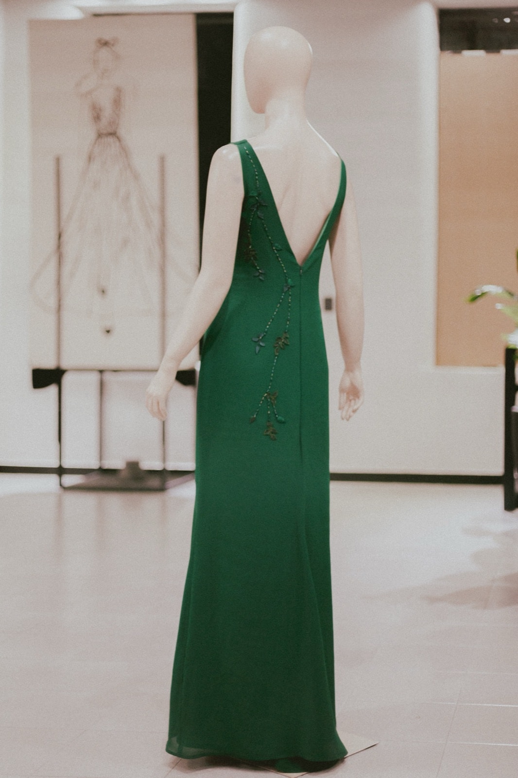 Vestido largo verde sobre maniquí en el showroom, vista trasera completa con el bordado de ramas recorriendo la espalda y la falda.