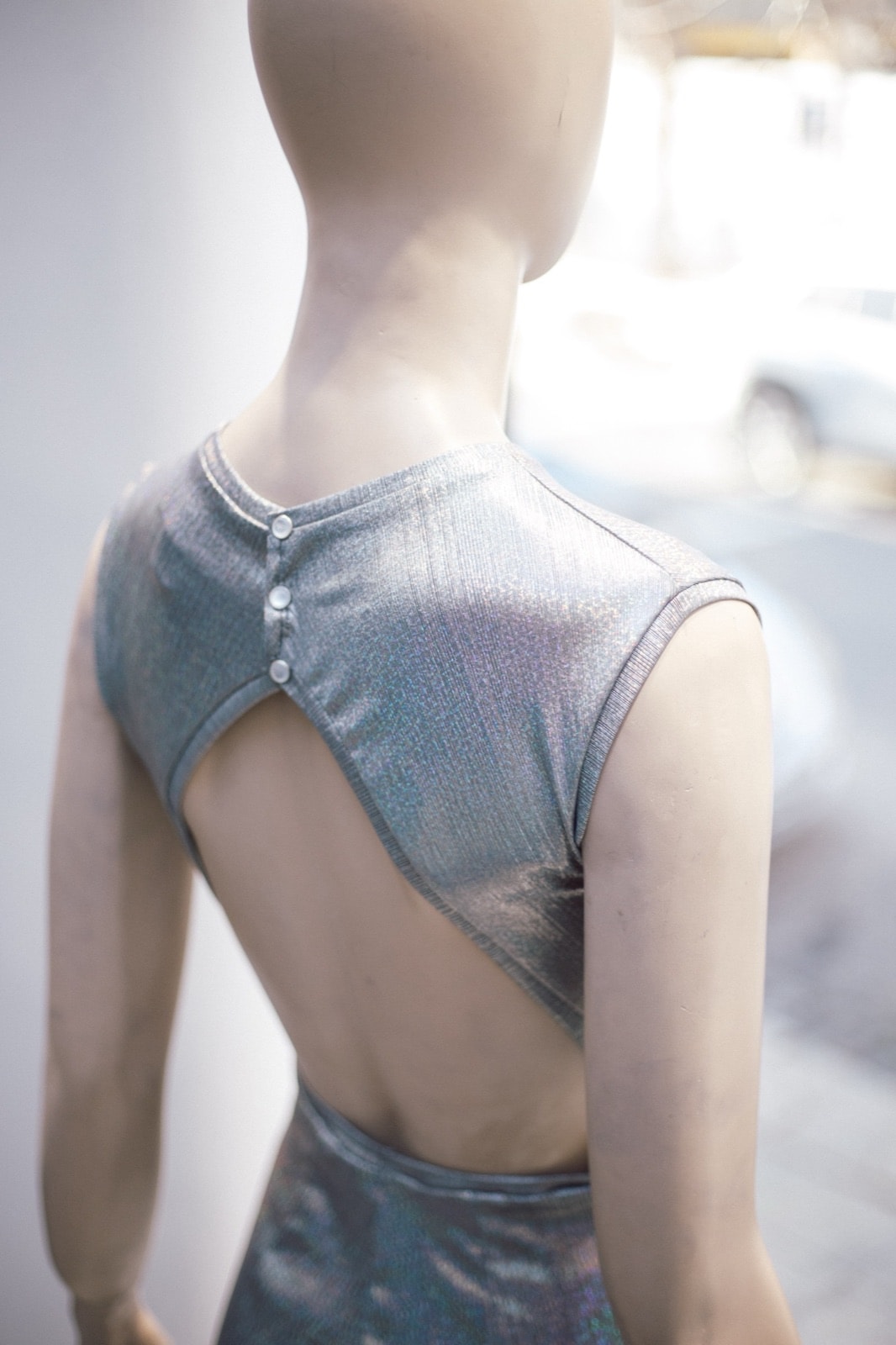 Detalle de la espalda del mono plateado holográfico, con recorte triangular y botones metálicos sobre maniquí.
