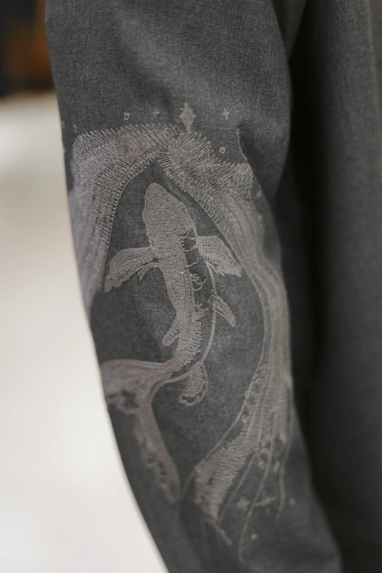 Detalle del bordado tono sobre tono de un pez en el brazo del jumpsuit sastrero gris, con hilos que imitan destellos de agua.